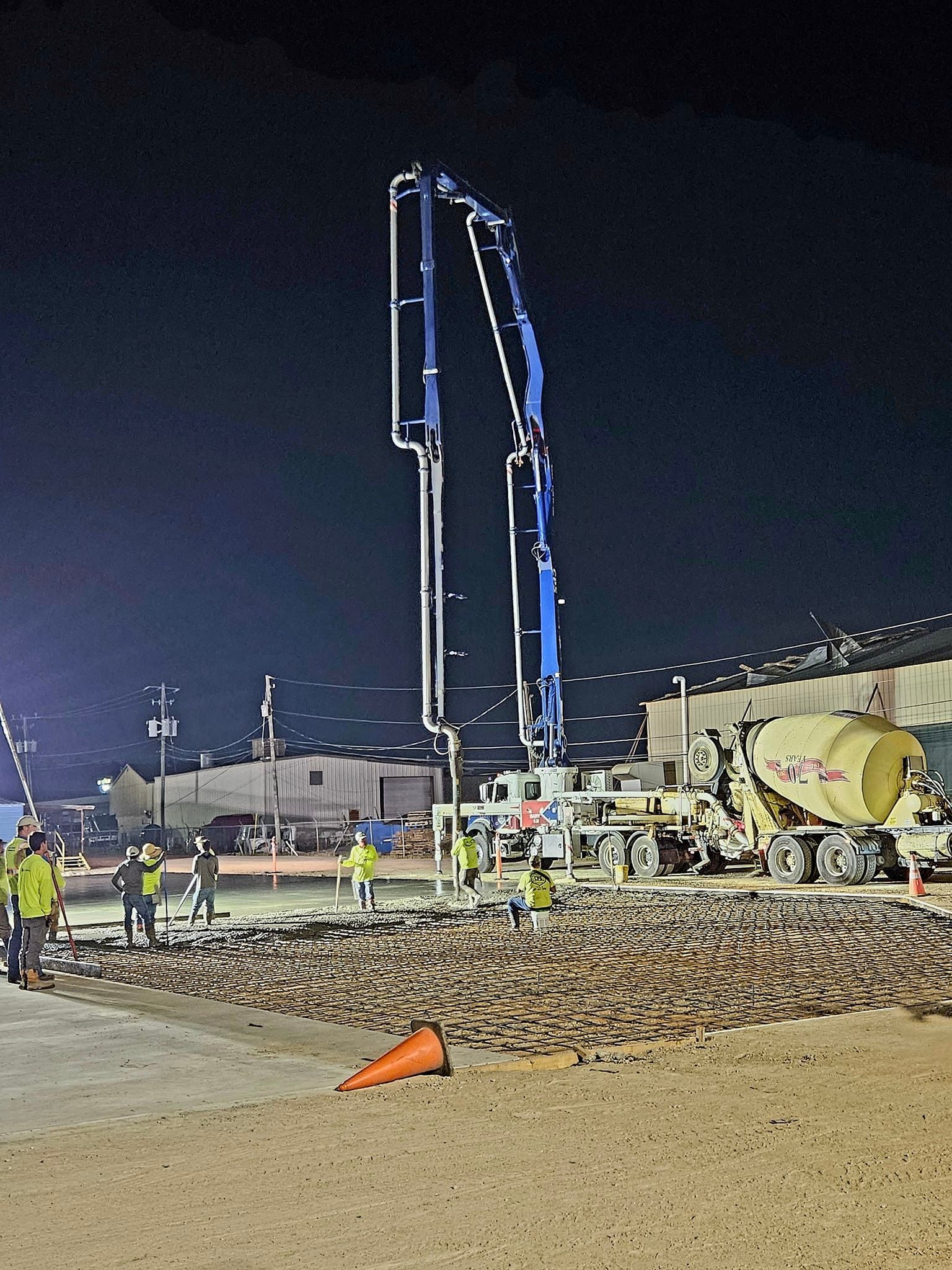 A concrete pump is being used to pour concrete on a construction site at night.
