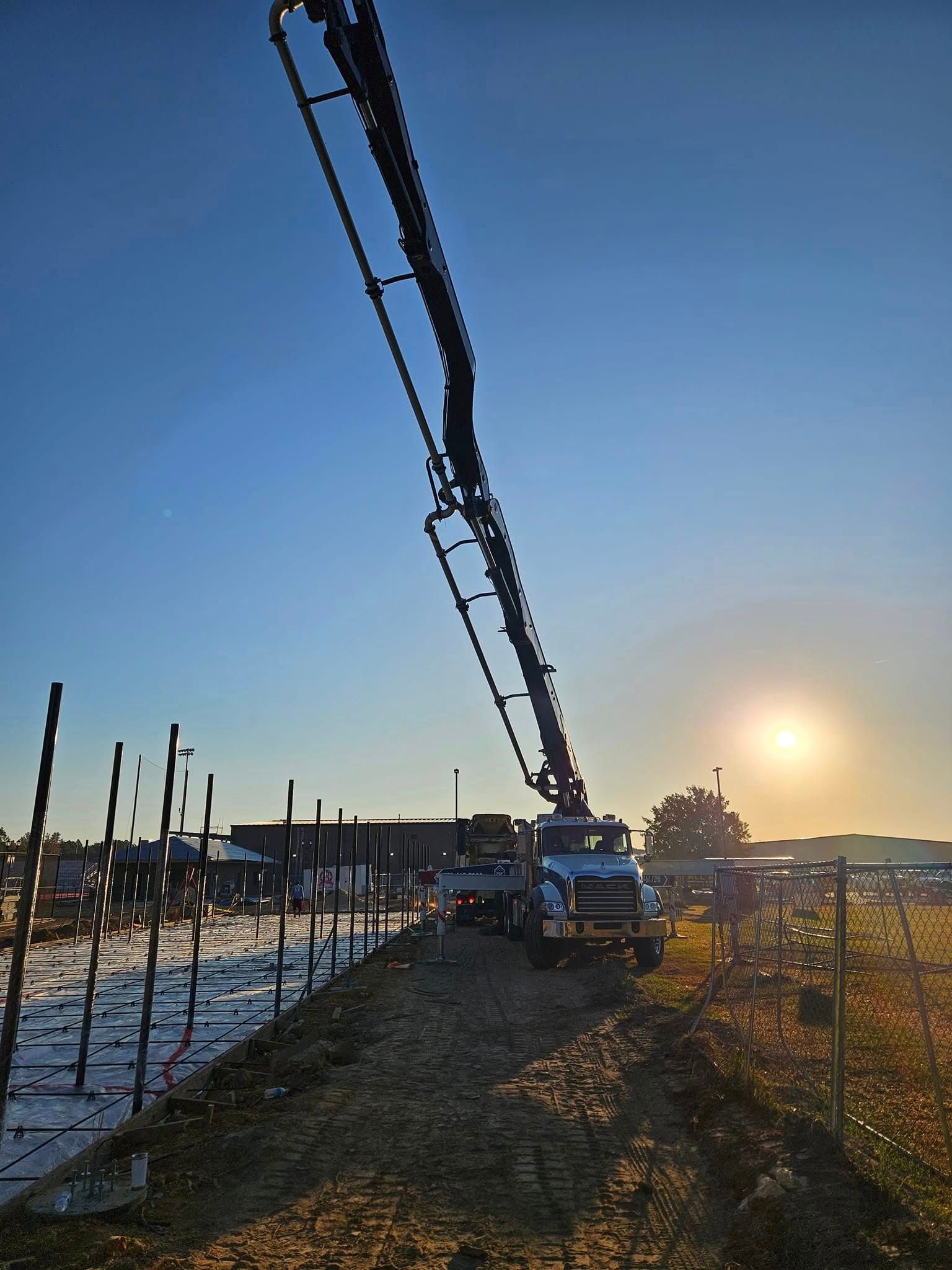 A concrete pump is being used to pour concrete into a fenced in area.