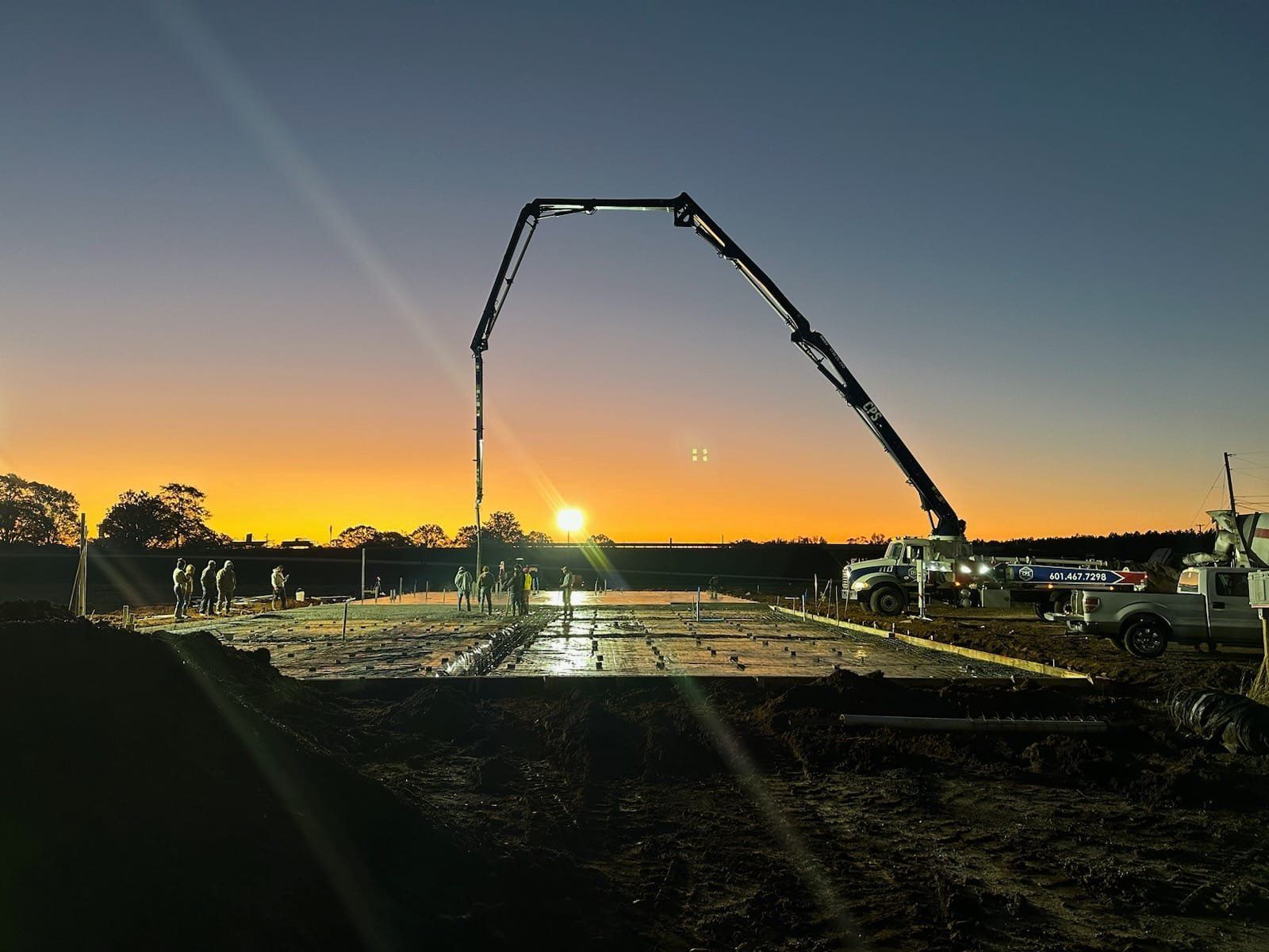 A construction site with a crane pumping concrete at sunset.