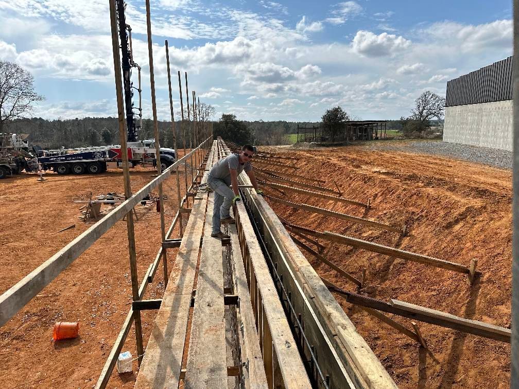 A man is standing on a wooden platform in a dirt field.