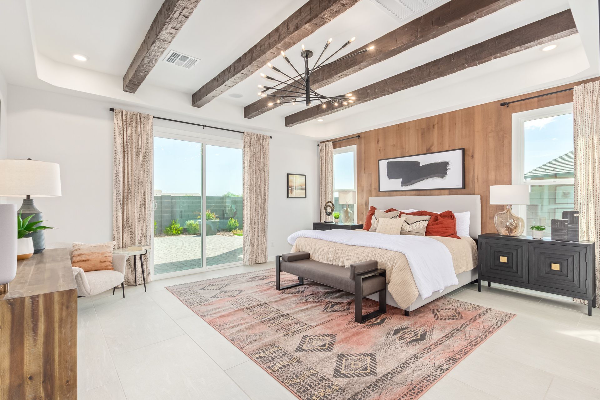 A bedroom with a bed , dresser , chair , rug and sliding glass doors.