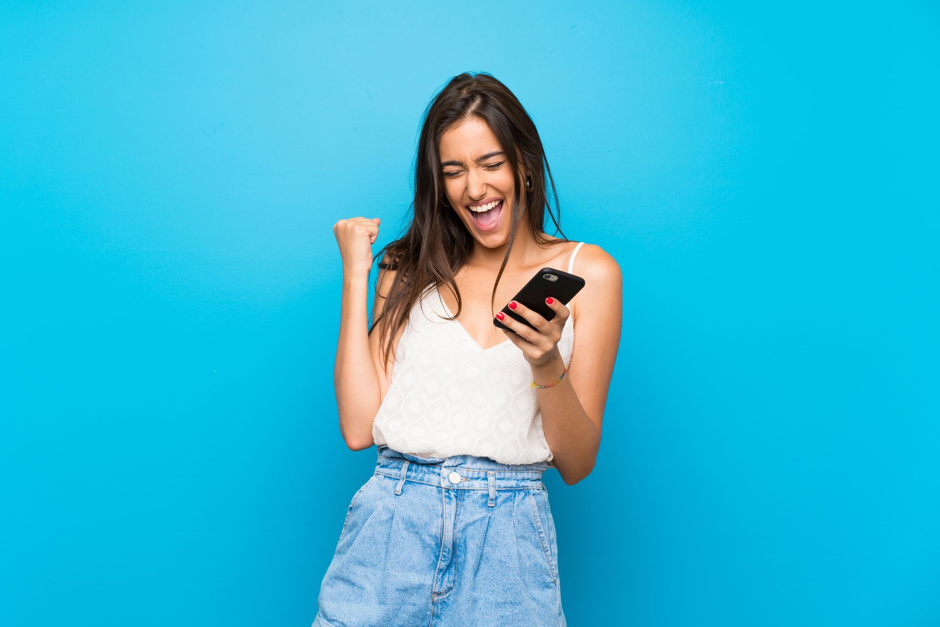 Woman with a phone, celebrating, fist raised, excited expression, against a blue background.