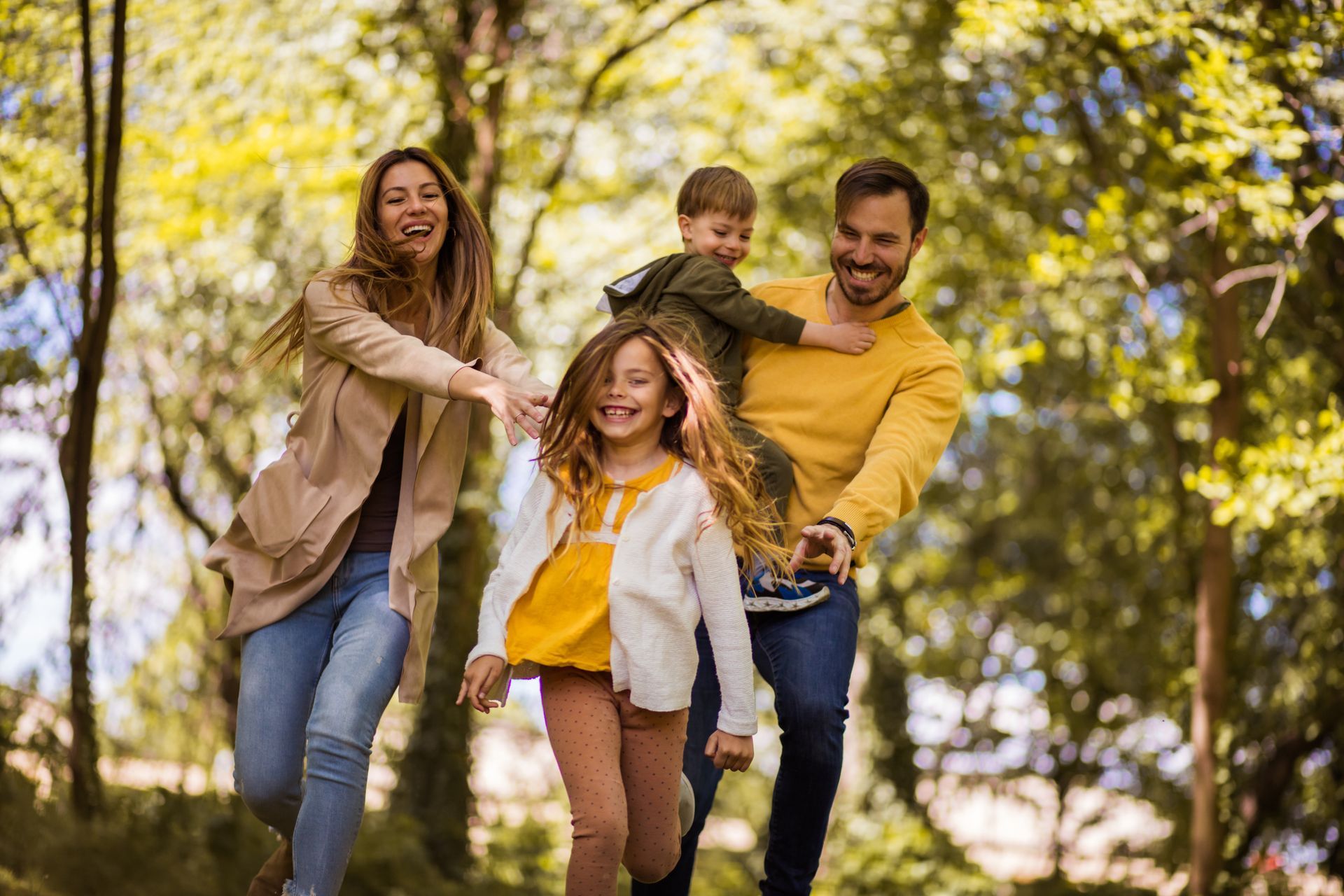 Family running and laughing in a park with trees; autumn colors.