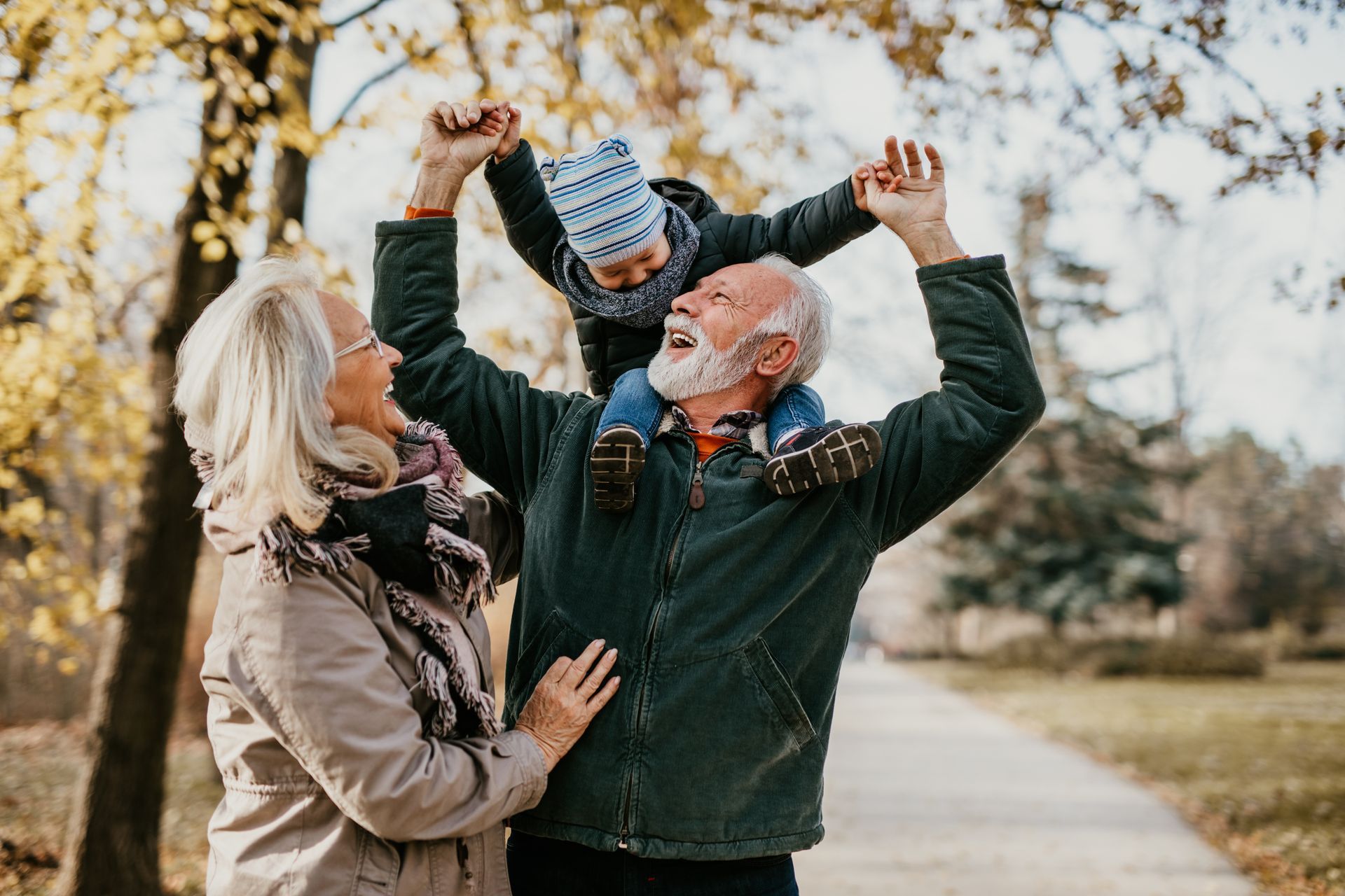 Grandfather carrying a child on his shoulders, smiling with grandmother in autumn park.