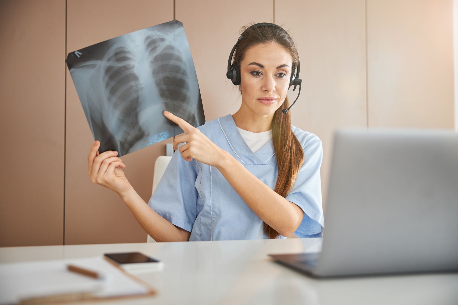 Doctor with headset showing lung X-ray on video call.