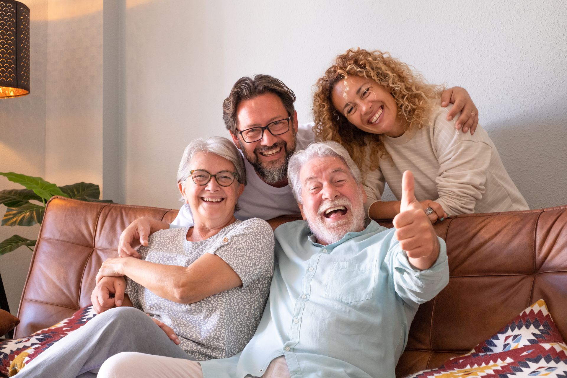 Four smiling people of varying ages on a brown couch.  One gives a thumbs up.