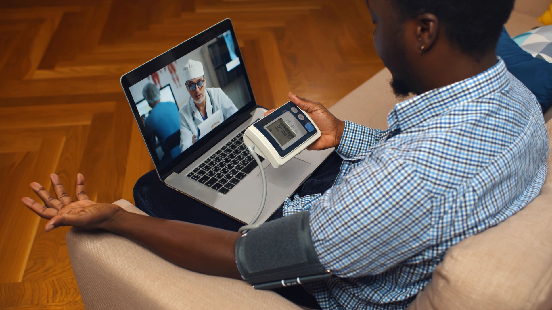 Man using blood pressure monitor during a telehealth appointment on a laptop.