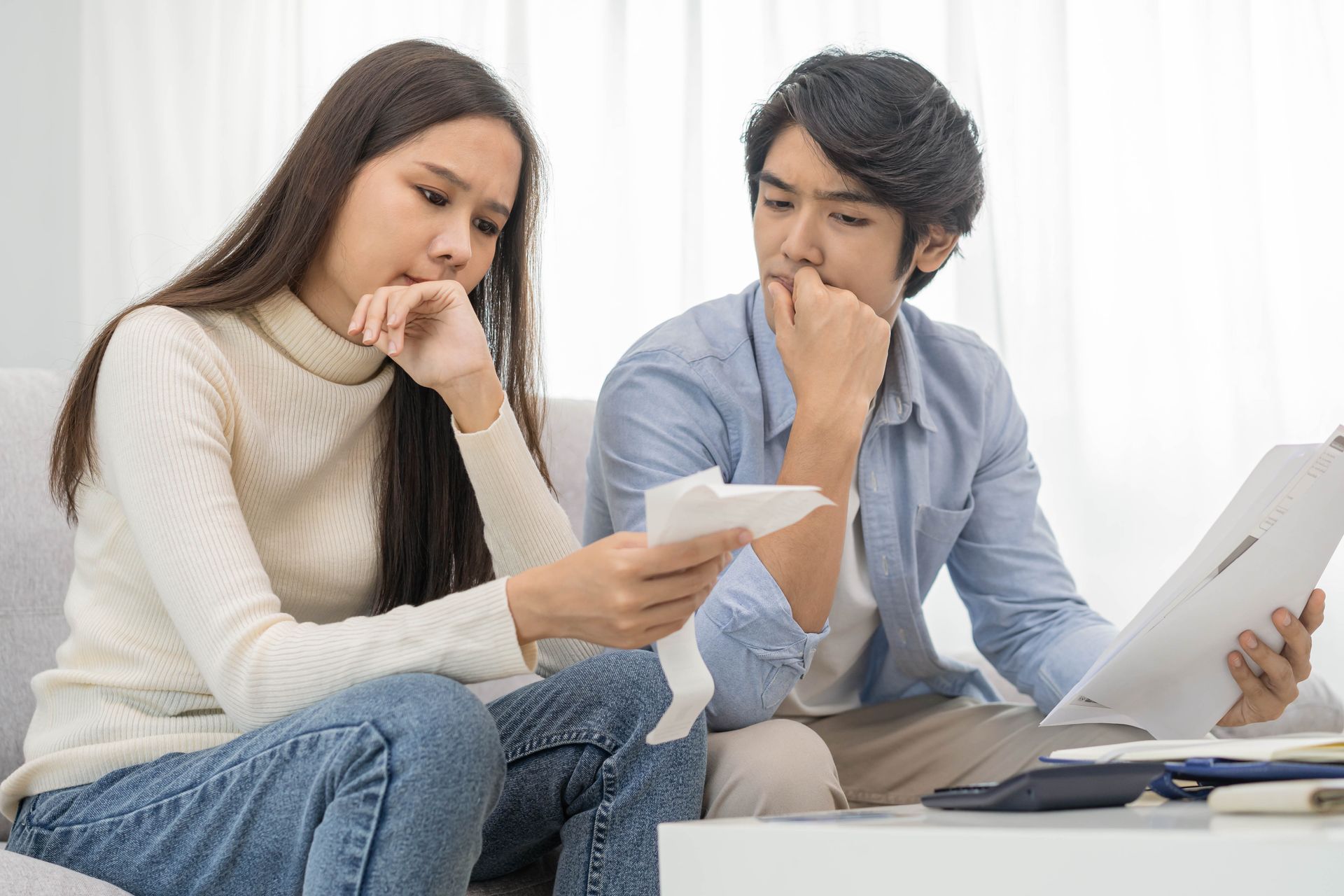 Couple looking at bills, appearing concerned while sitting on a couch.