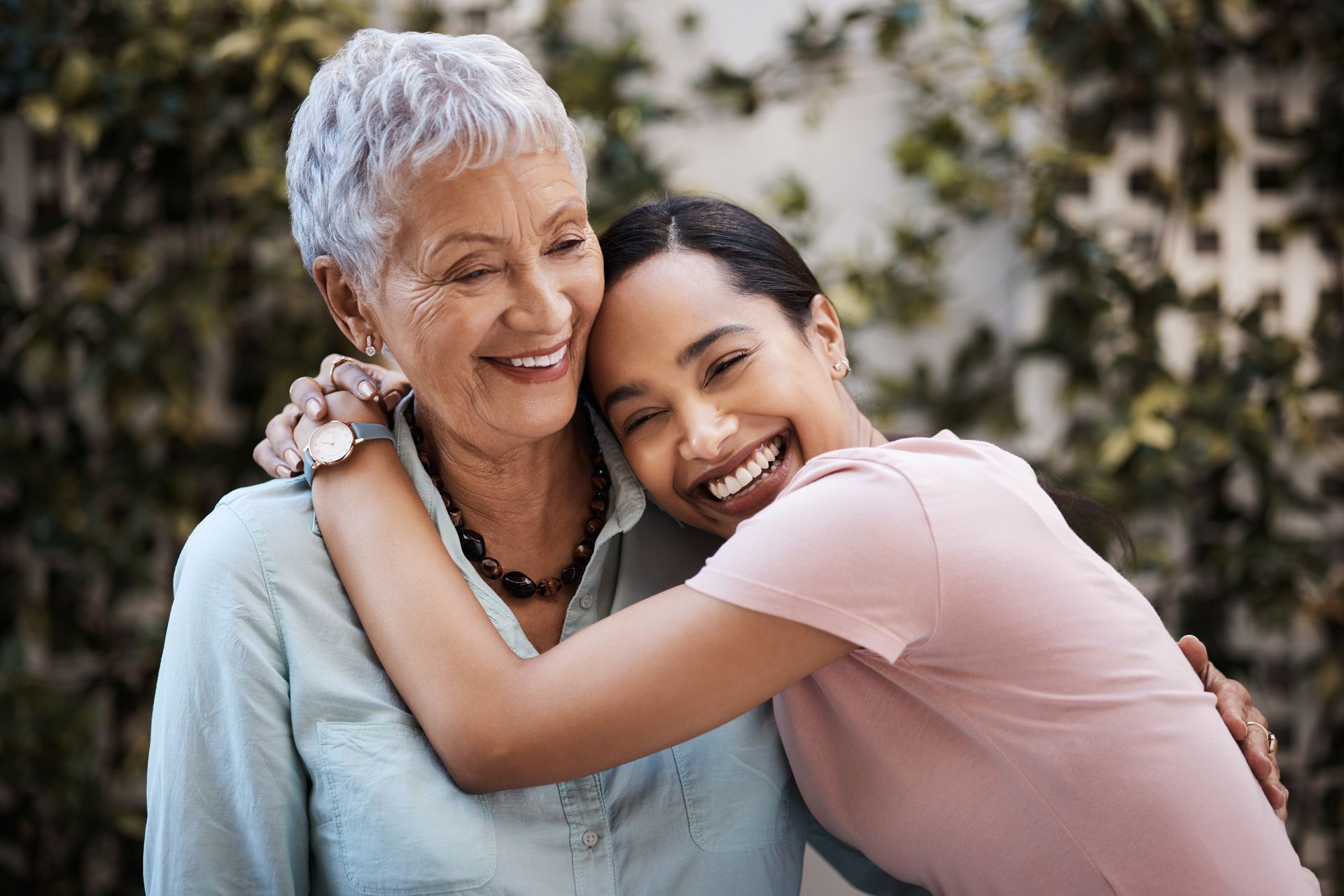 Woman embraces an older woman, both smiling outdoors.