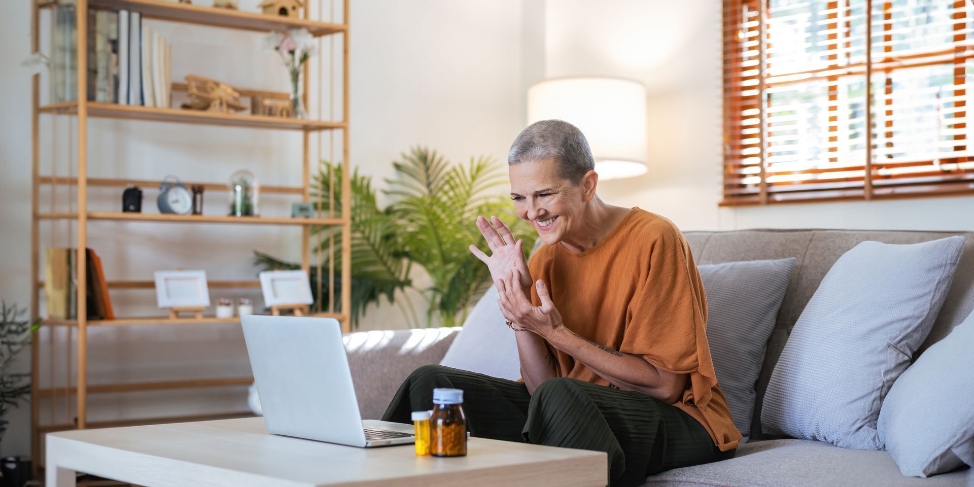 Woman on a couch, waving at a laptop, with medication on a table.