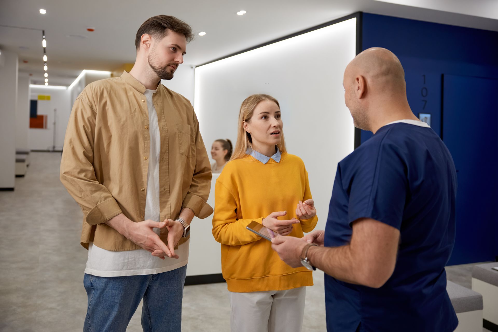 Couple talking with a doctor in a modern hallway. The woman gestures while the man listens.