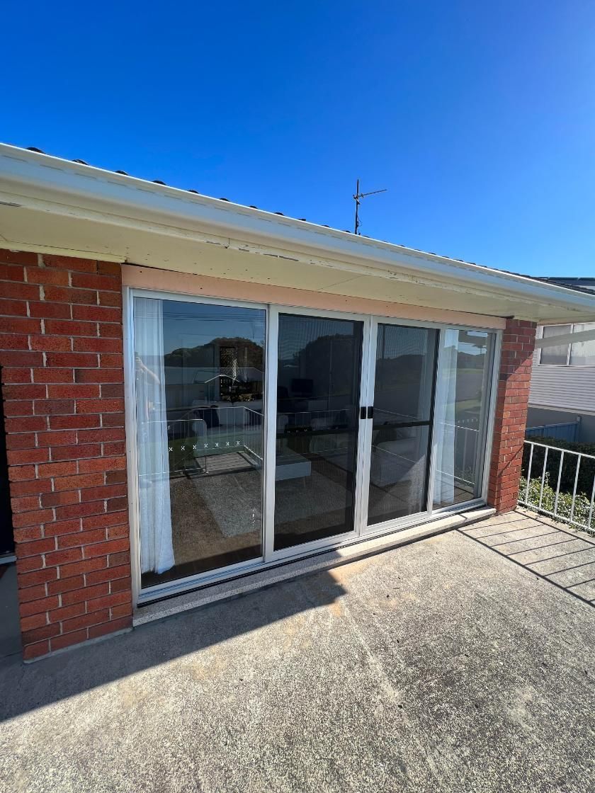 A Brick House With Sliding Glass Doors And A Blue Sky In The Background — Glass 24/7 In Forster, NSW