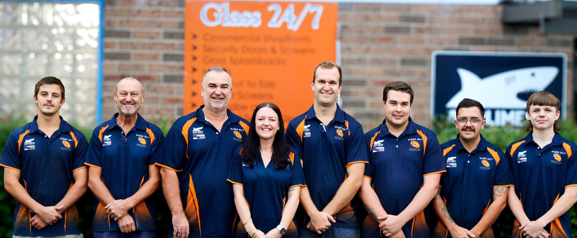 A group of people standing in front of a sign that says class 24/1 — Glass 24/7 In Taree, NSW