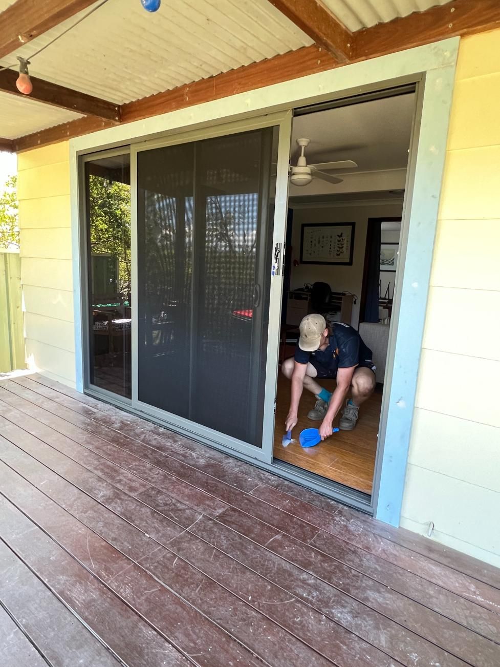 A Man Is Cleaning A Sliding Glass Door On A Deck — Glass 24/7 In Tuncurry, NSW