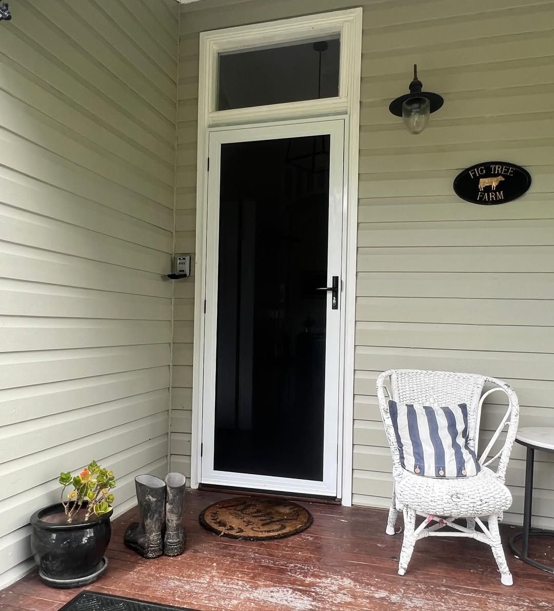 A Wicker Chair Sits On A Porch Next To A Glass Door — Glass 24/7 In Hallidays Point, NSW