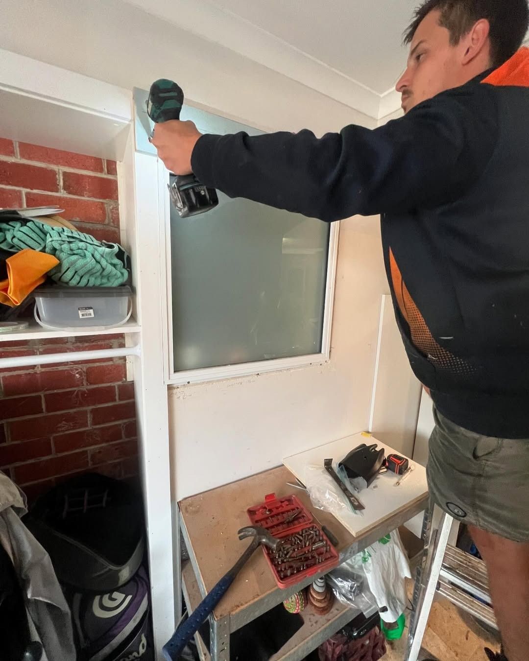 A Man Is Using A Drill To Fix A Window In A Closet — Glass 24/7 In Tuncurry, NSW