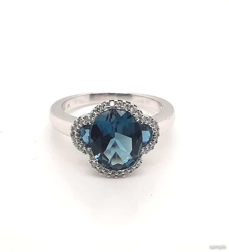 Silver ring with a large blue gemstone center, surrounded by smaller gemstones and a white band.