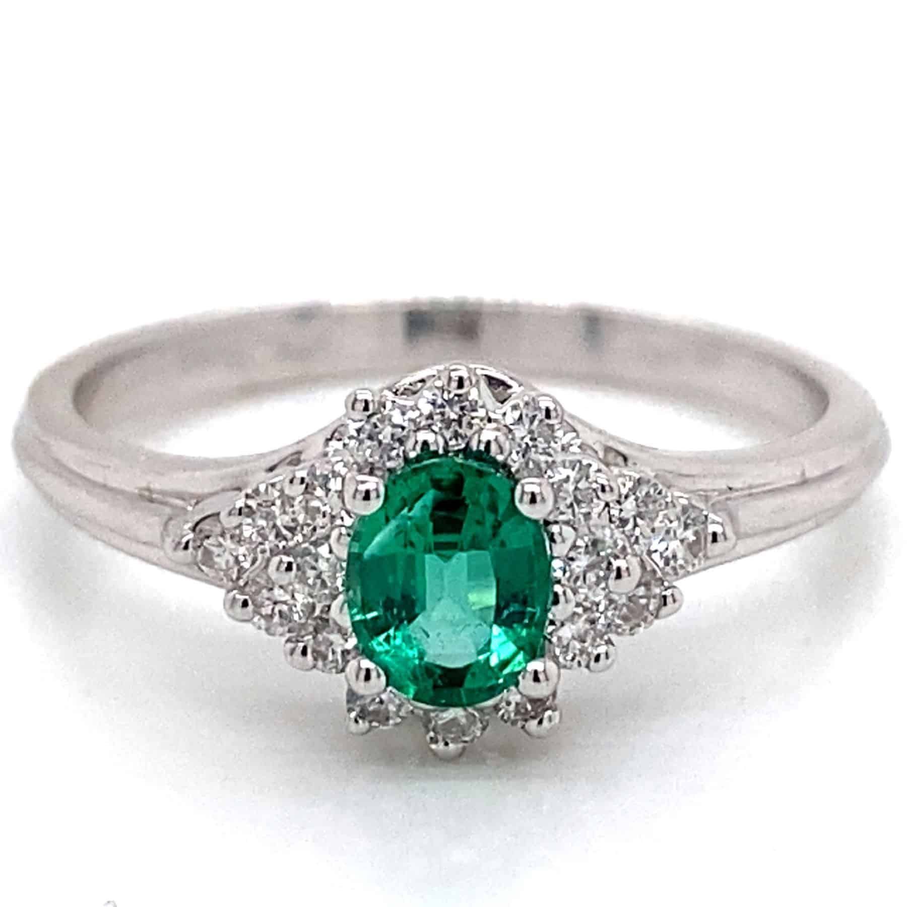 Oval emerald ring with diamond halo, set in white gold.
