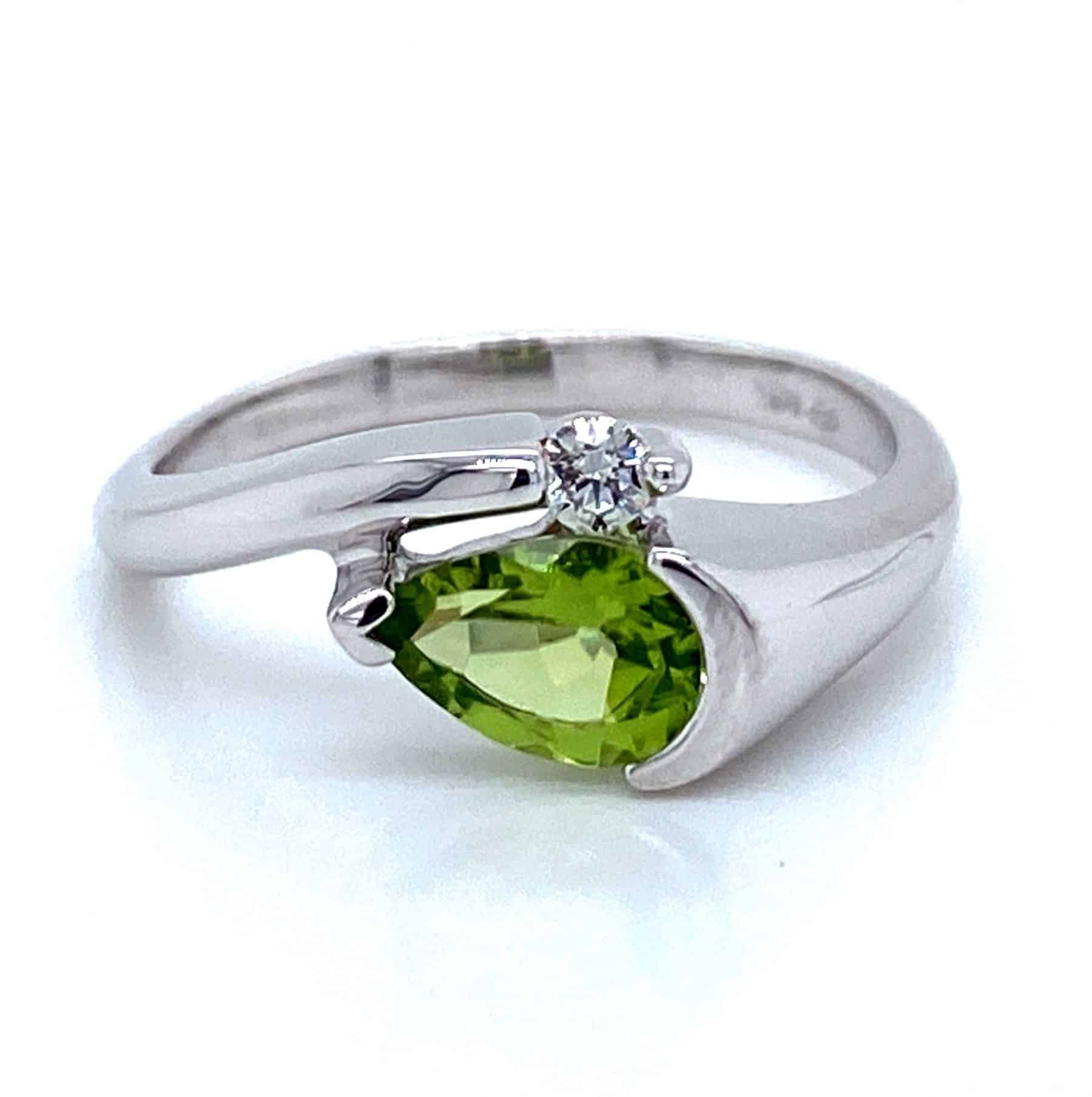 Silver ring with pear-shaped green gemstone and small white stone, angled on white.