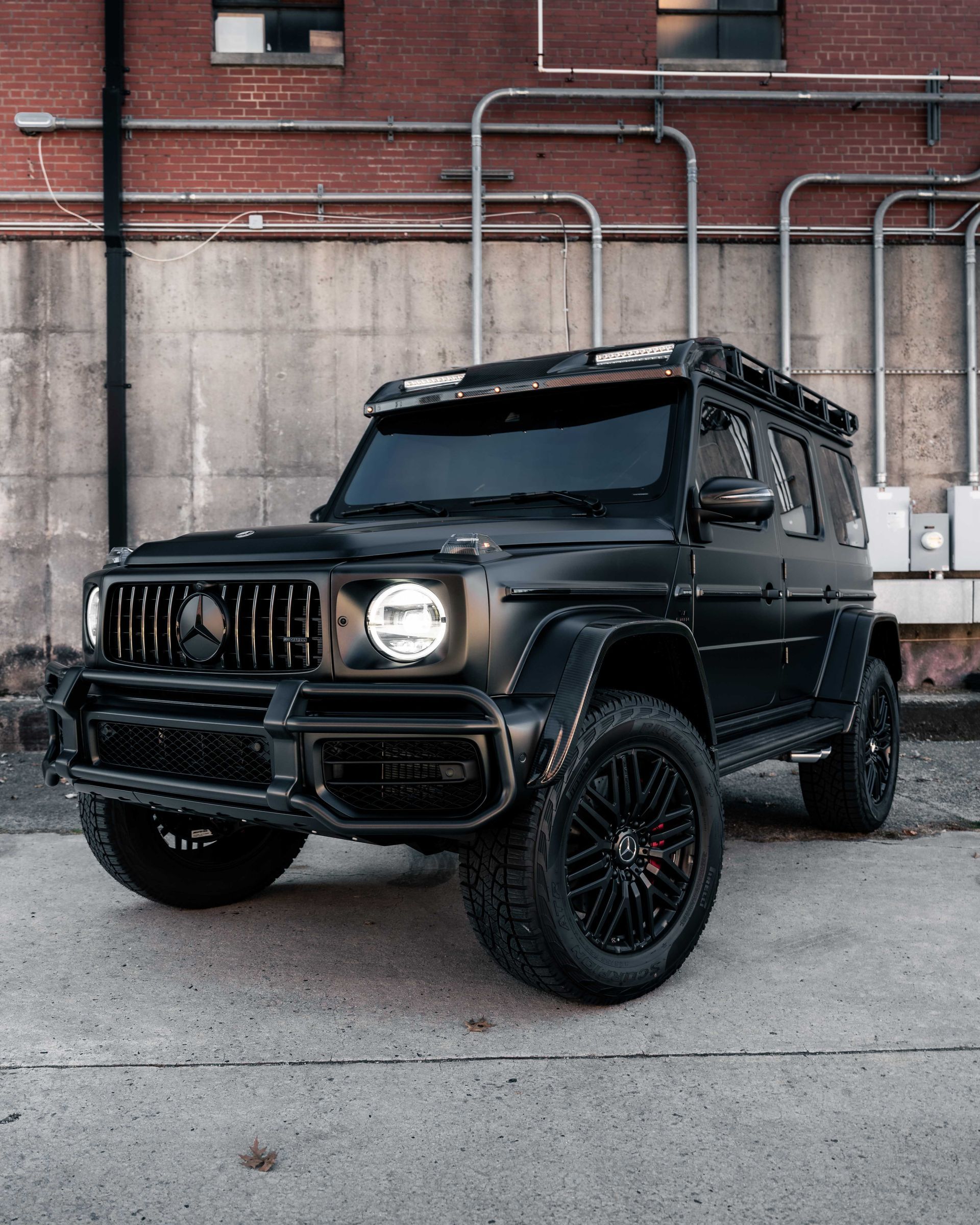 A black mercedes g63 is parked in front of a brick building.