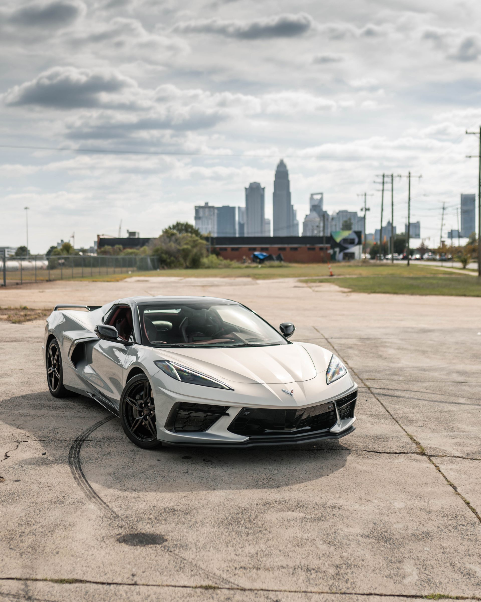 A white sports car is parked in a parking lot with a city skyline in the background.