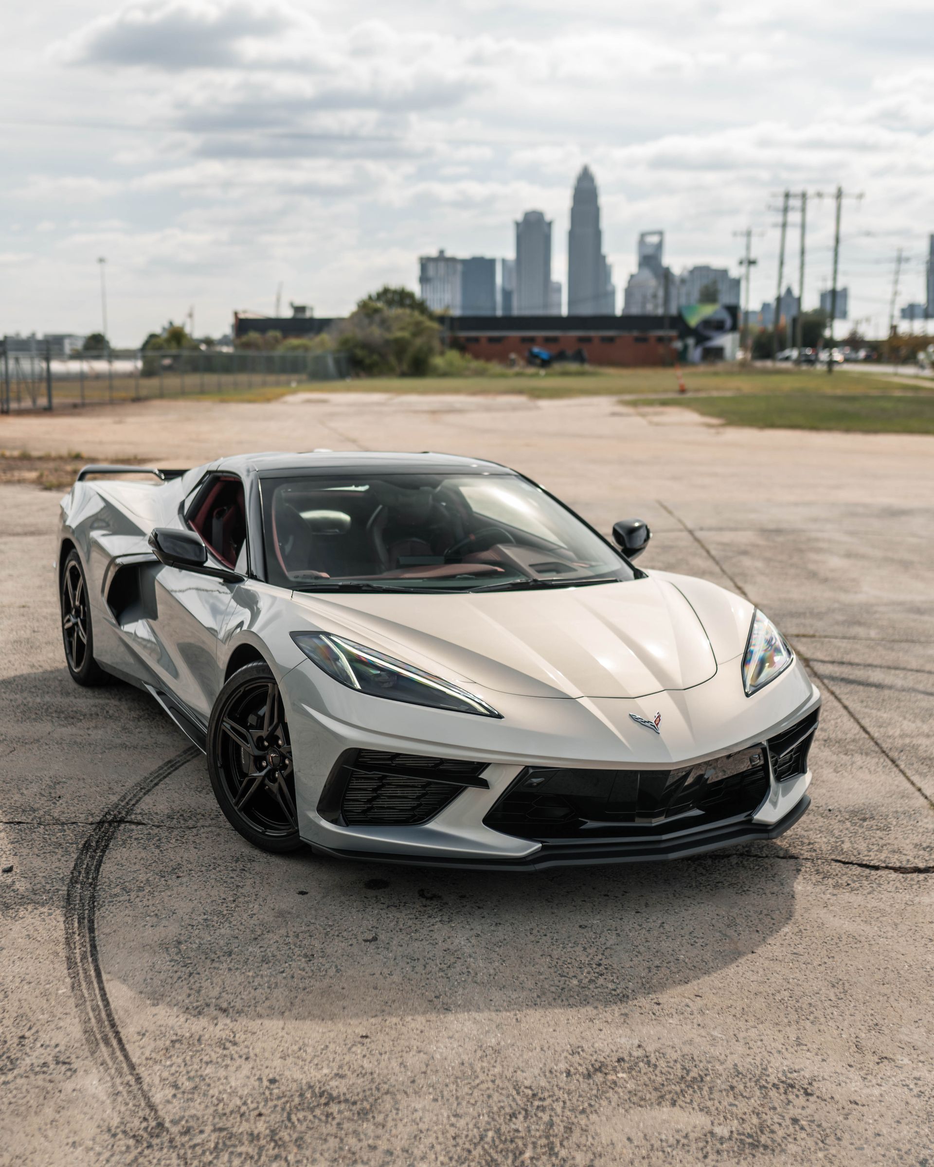 A silver sports car is parked in a parking lot with a city skyline in the background.