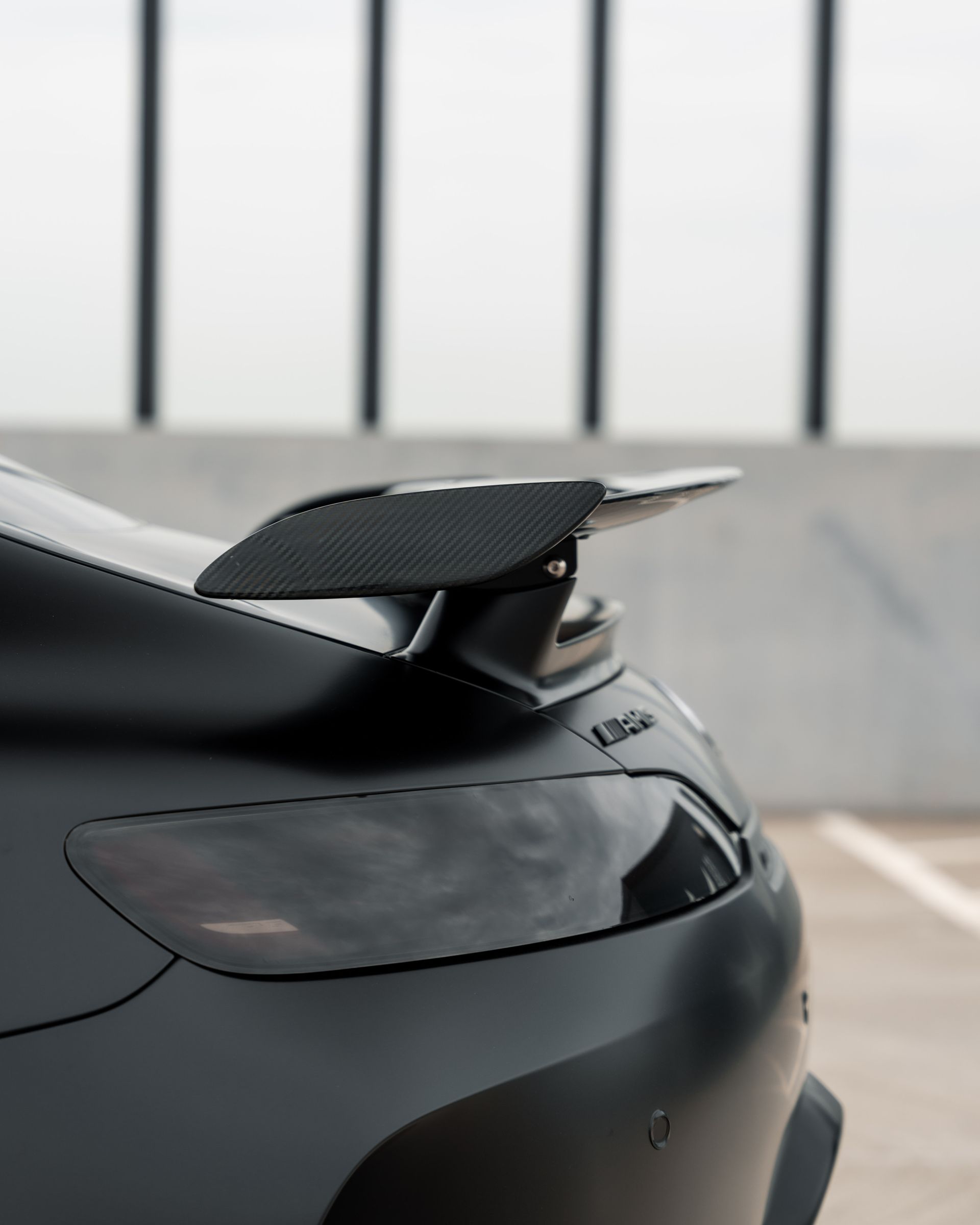 A black car with a spoiler on the back is parked in a parking lot.