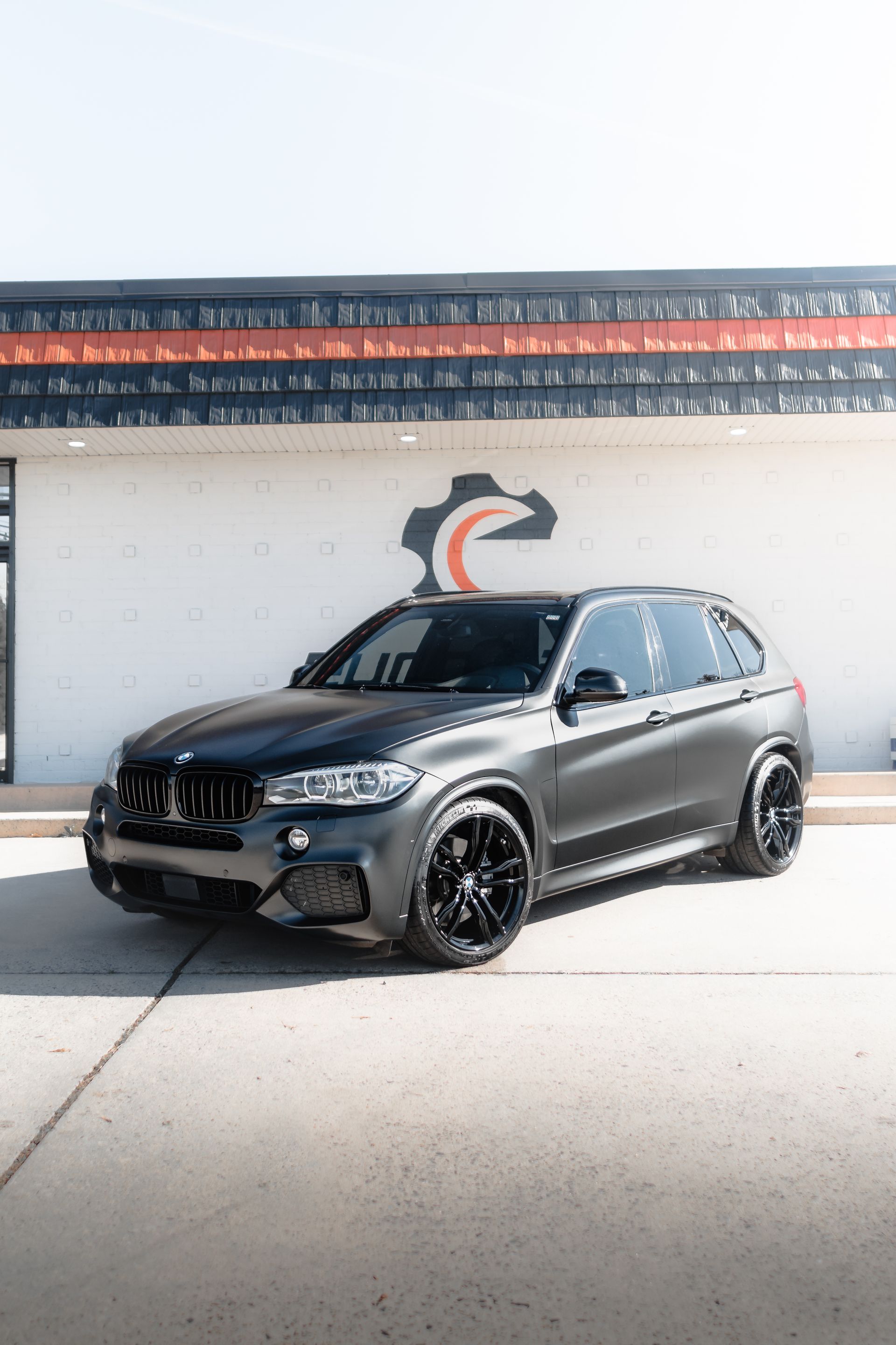 A black bmw x5 is parked in front of a building.
