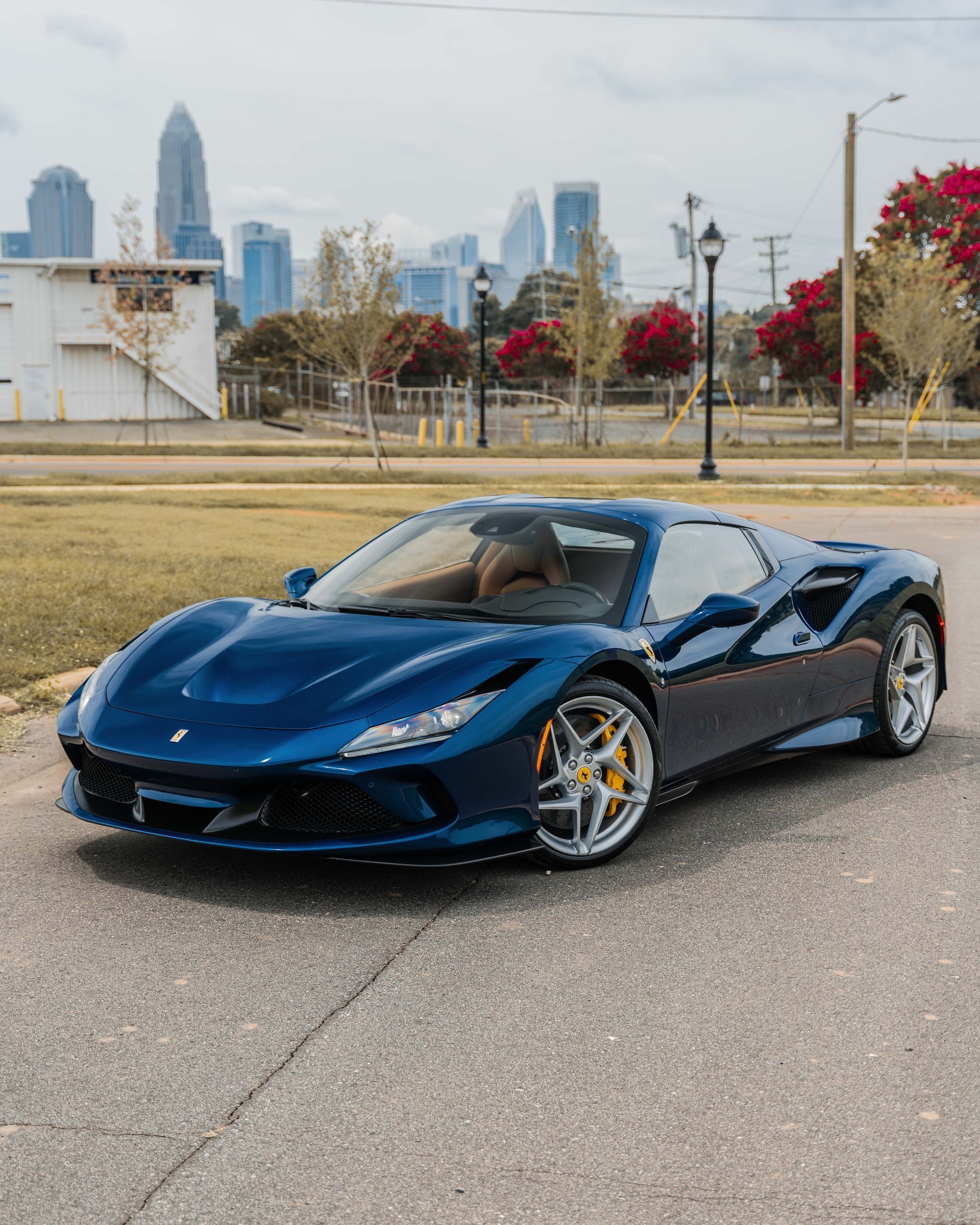 A blue sports car is parked on the side of the road in front of a city skyline.