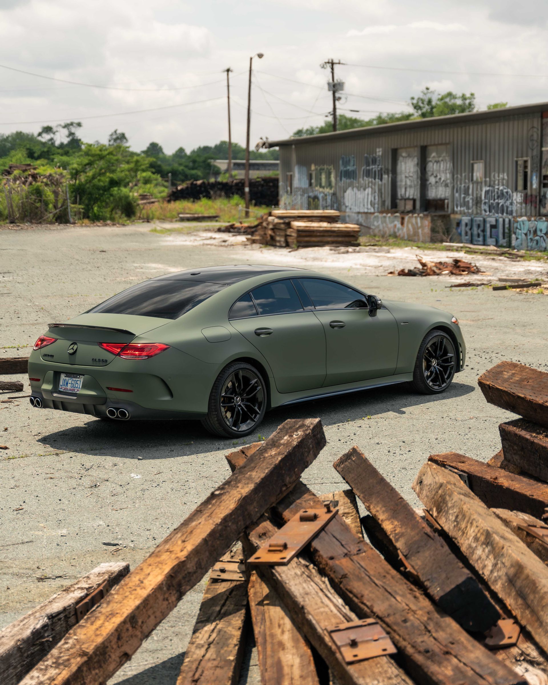 A green car is parked next to a pile of wood