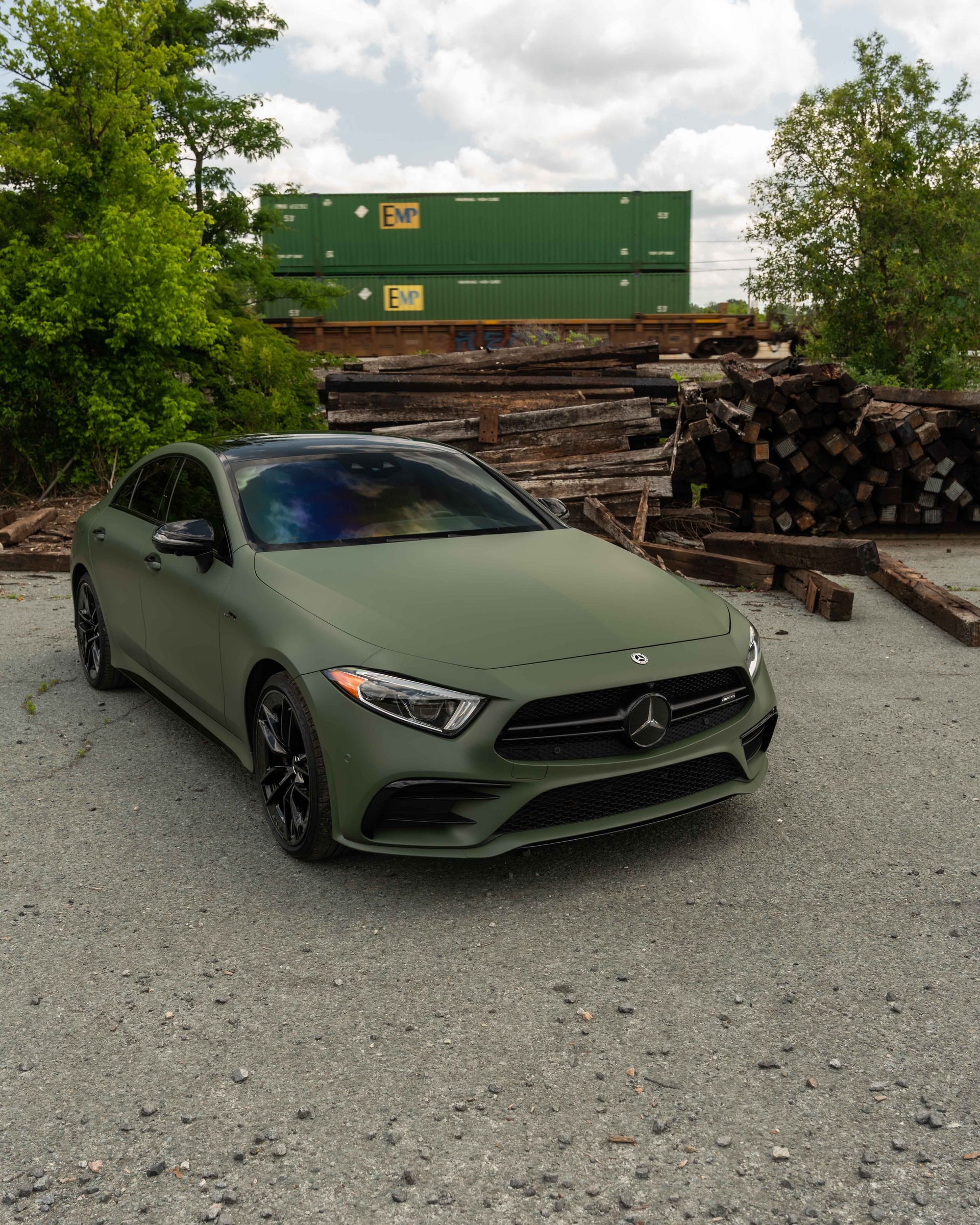 A green mercedes is parked in front of a pile of logs