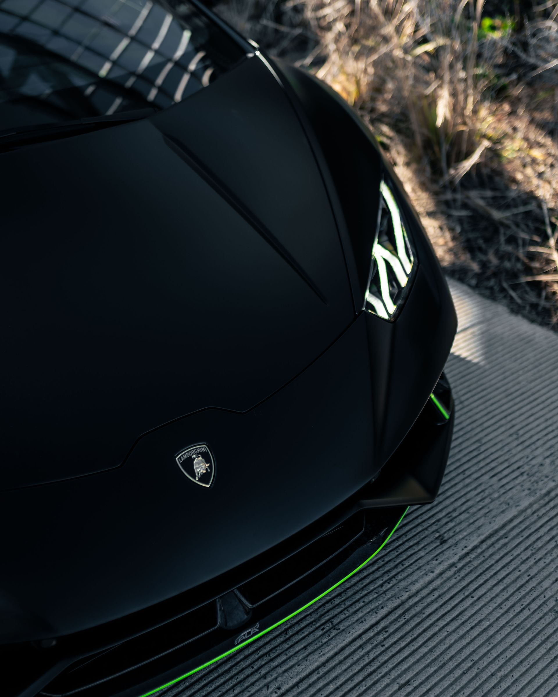 A black car with a green stripe on the front is parked on a sidewalk.