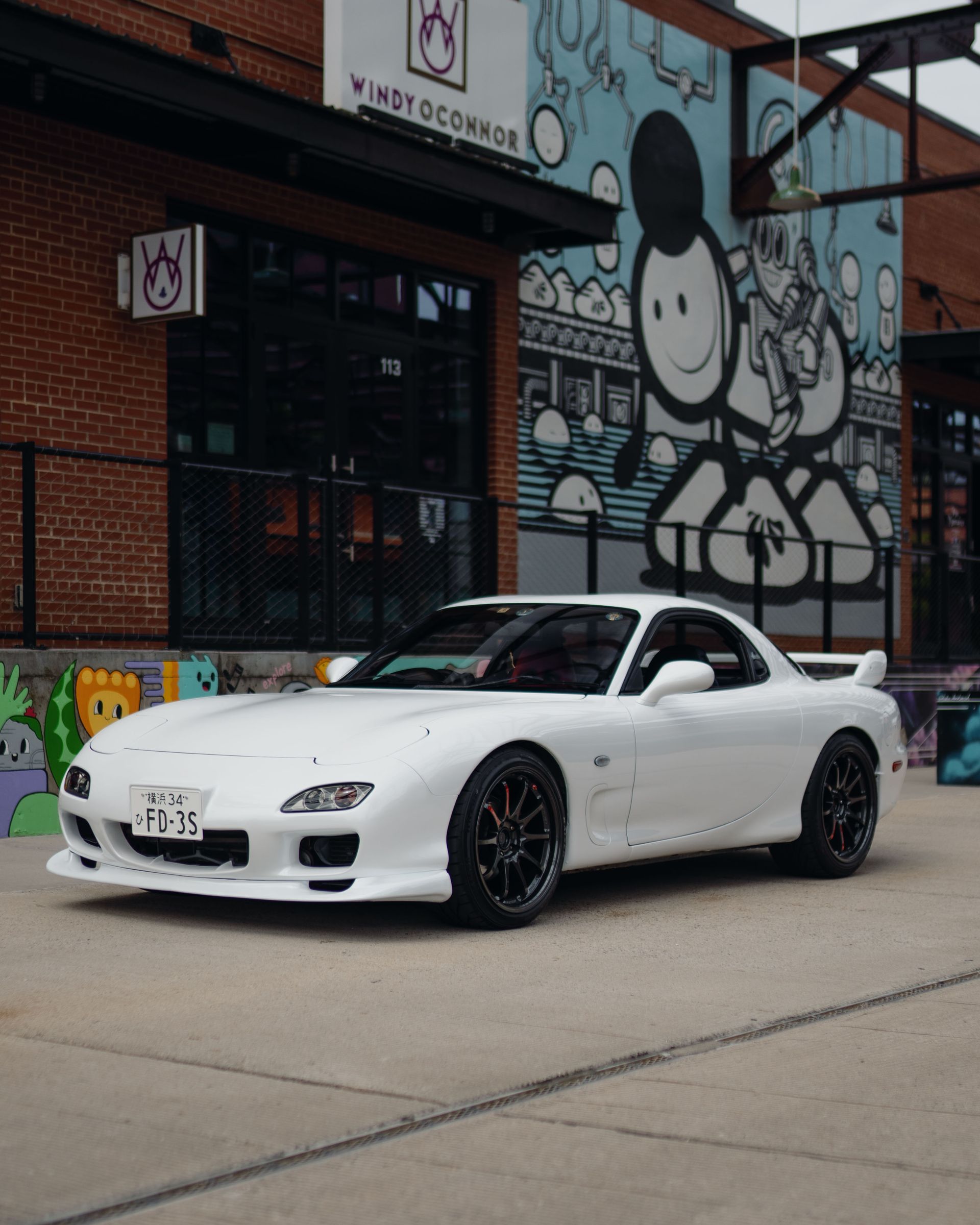 A white sports car is parked in front of a building with graffiti on it