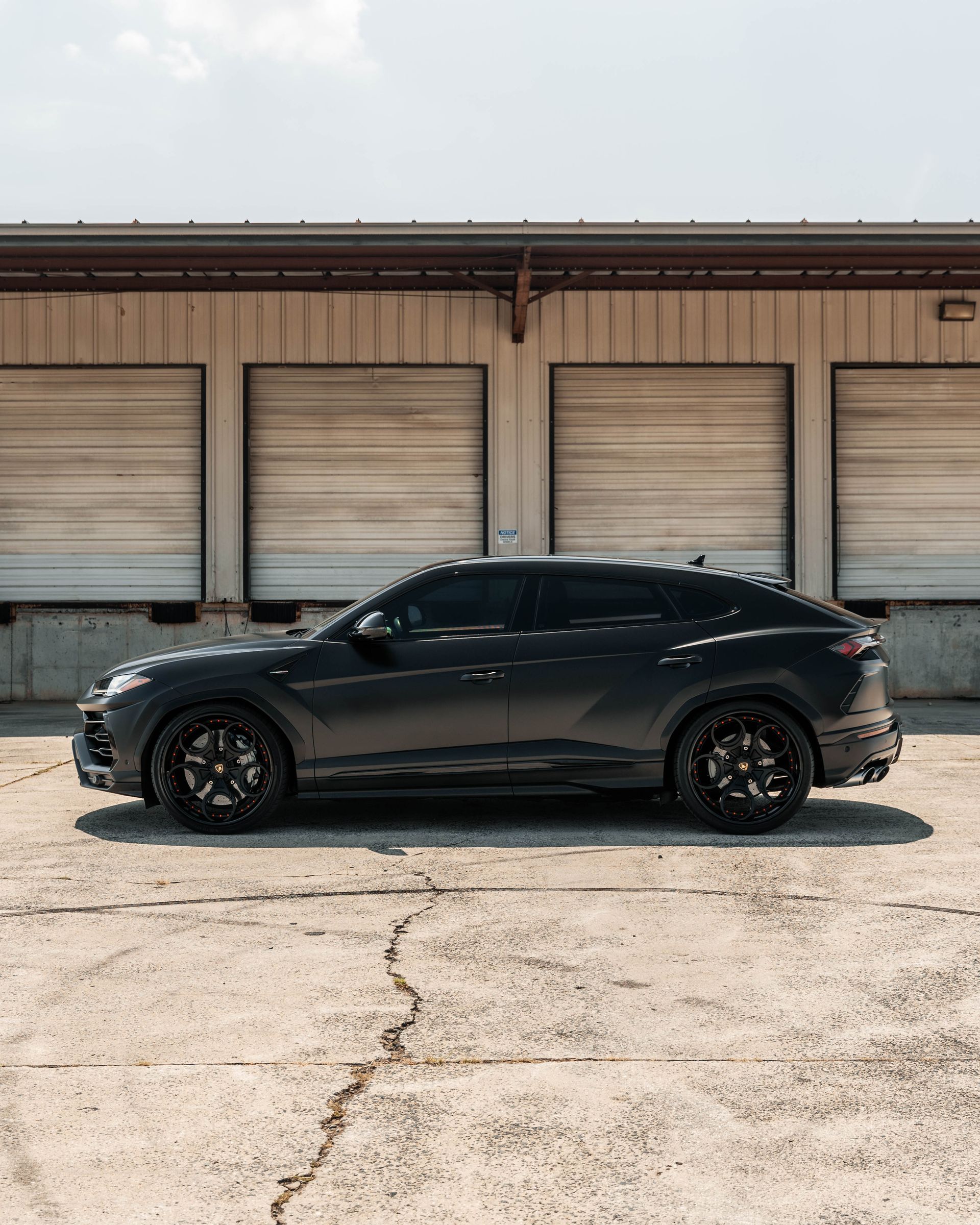 A black car is parked in front of a building with garage doors.