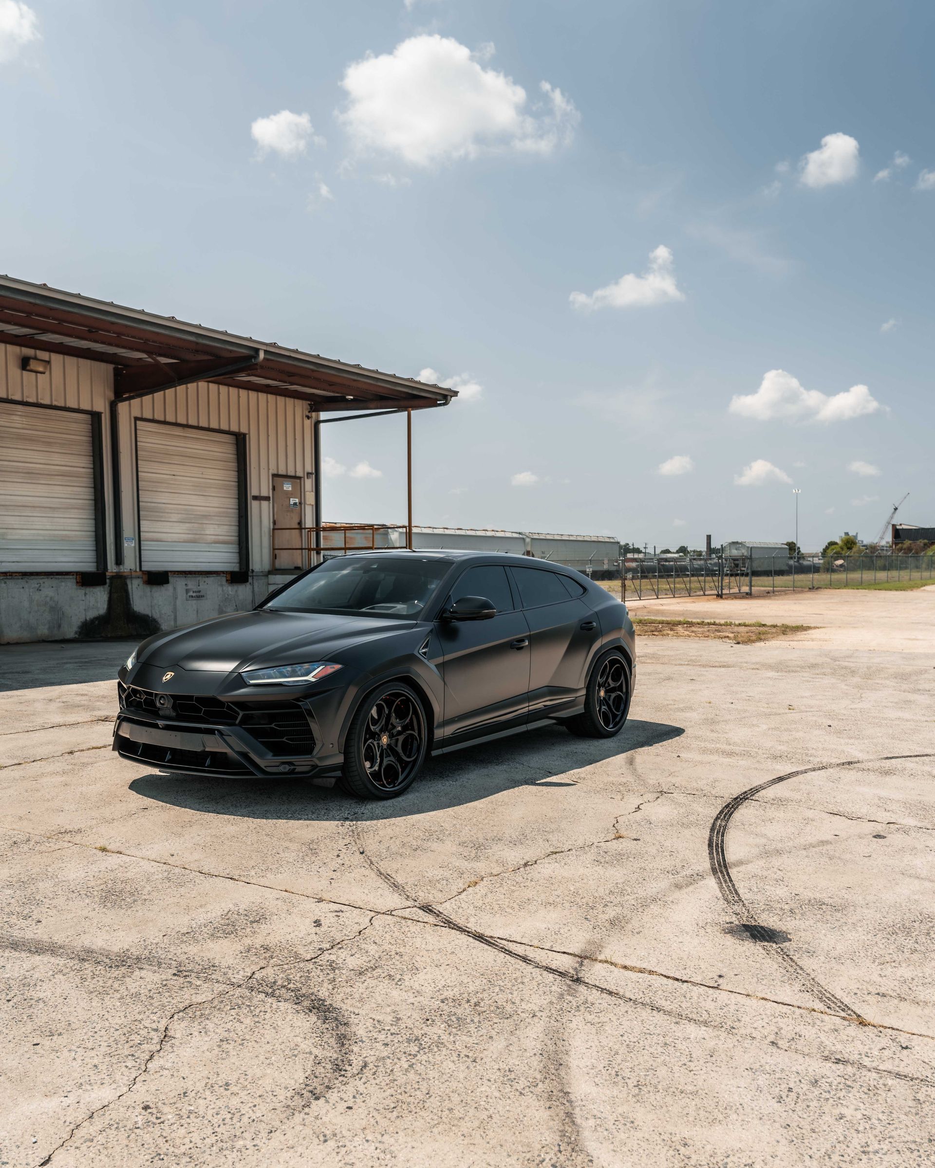 A black car is parked in a parking lot in front of a building.