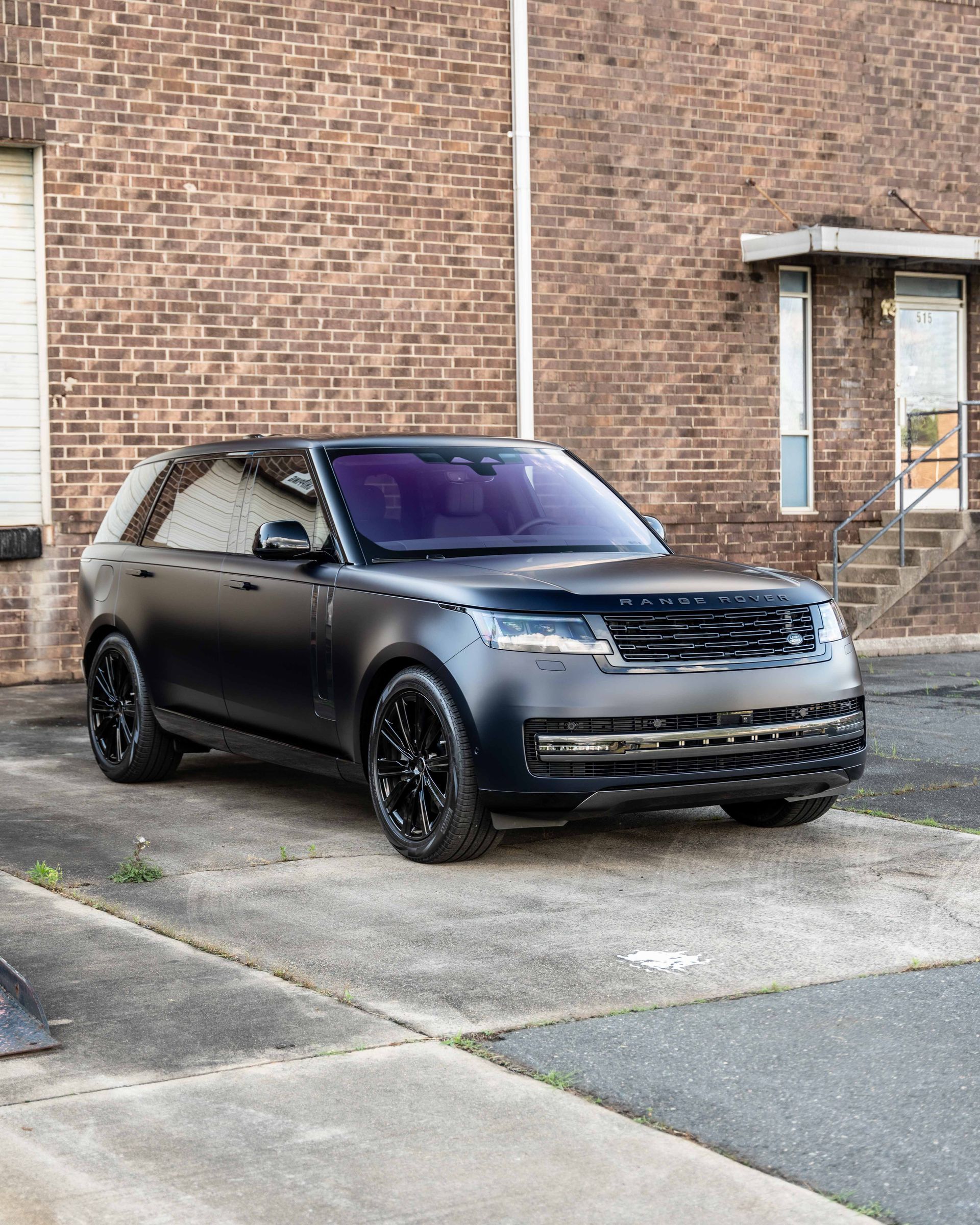 A black range rover is parked in front of a brick building.