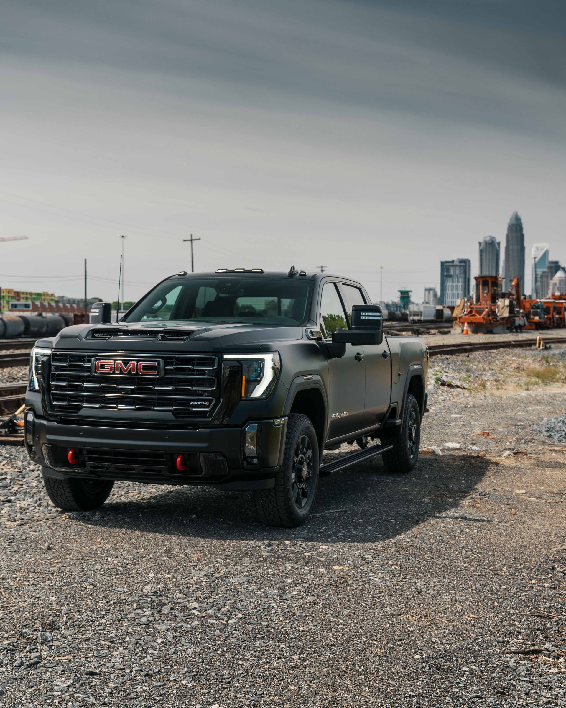 A black gmc truck is parked on a gravel road next to train tracks.