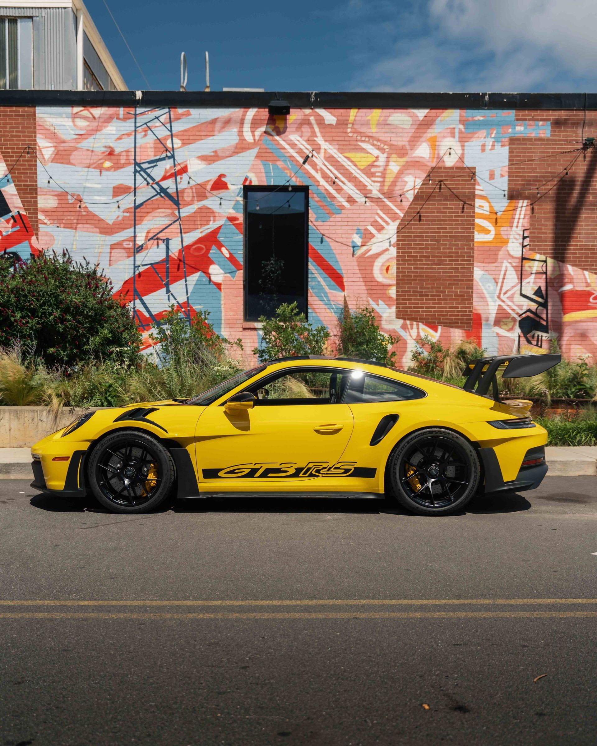 A yellow sports car is parked in front of a building with graffiti on it