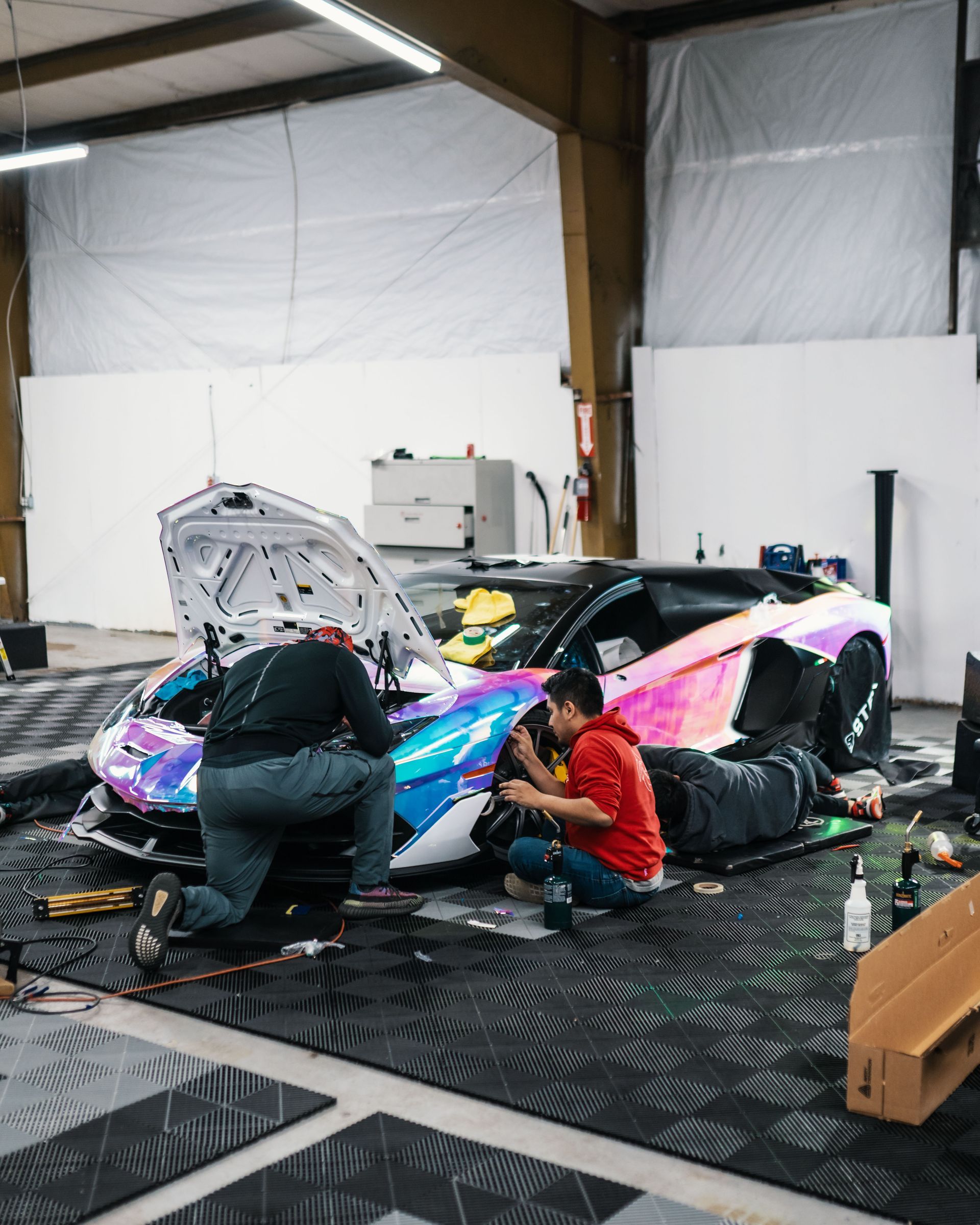 A group of men are working on a colorful sports car in a garage.