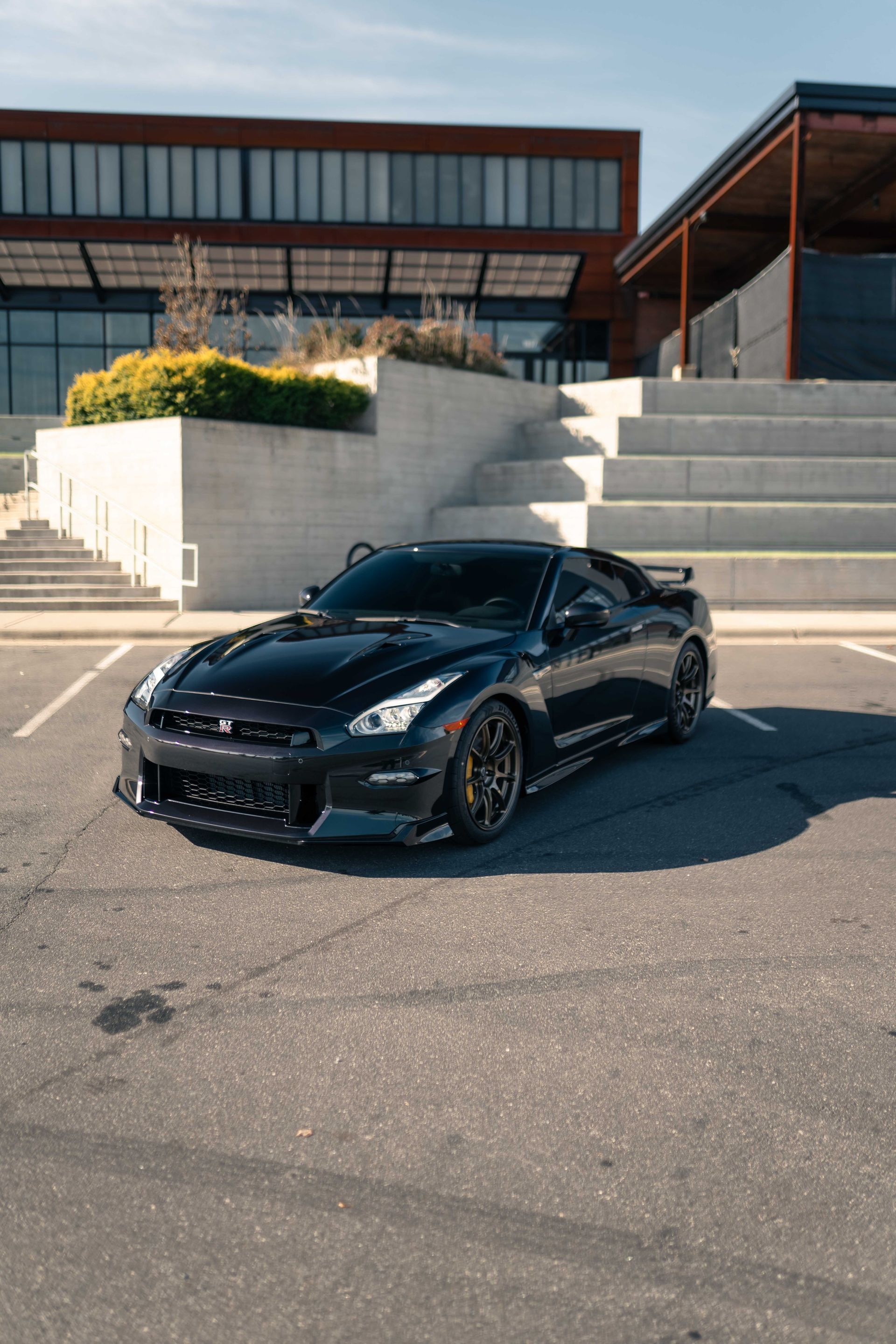 A black sports car is parked in a parking lot in front of a building.