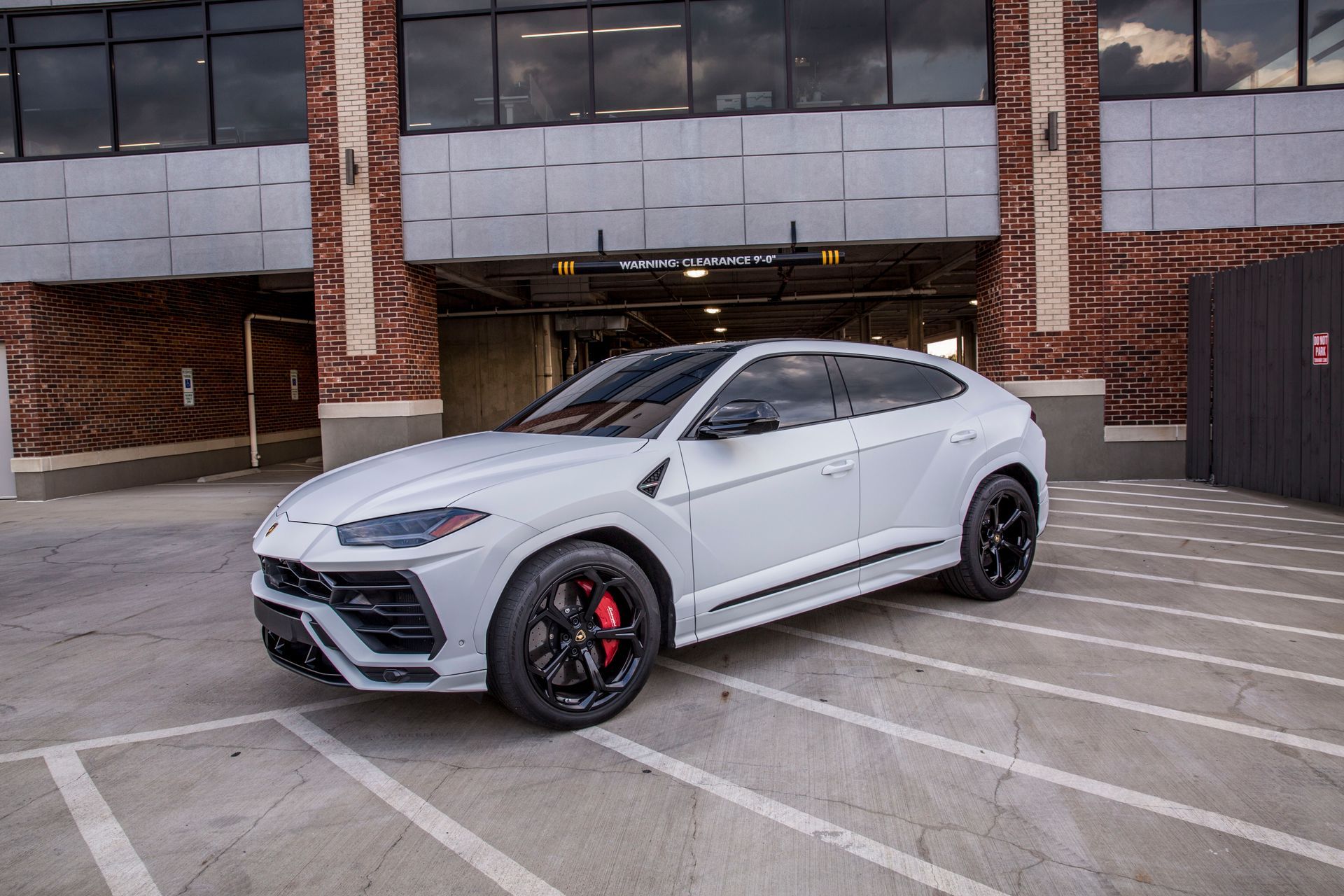 A white lamborghini urus is parked in a parking lot in front of a building.