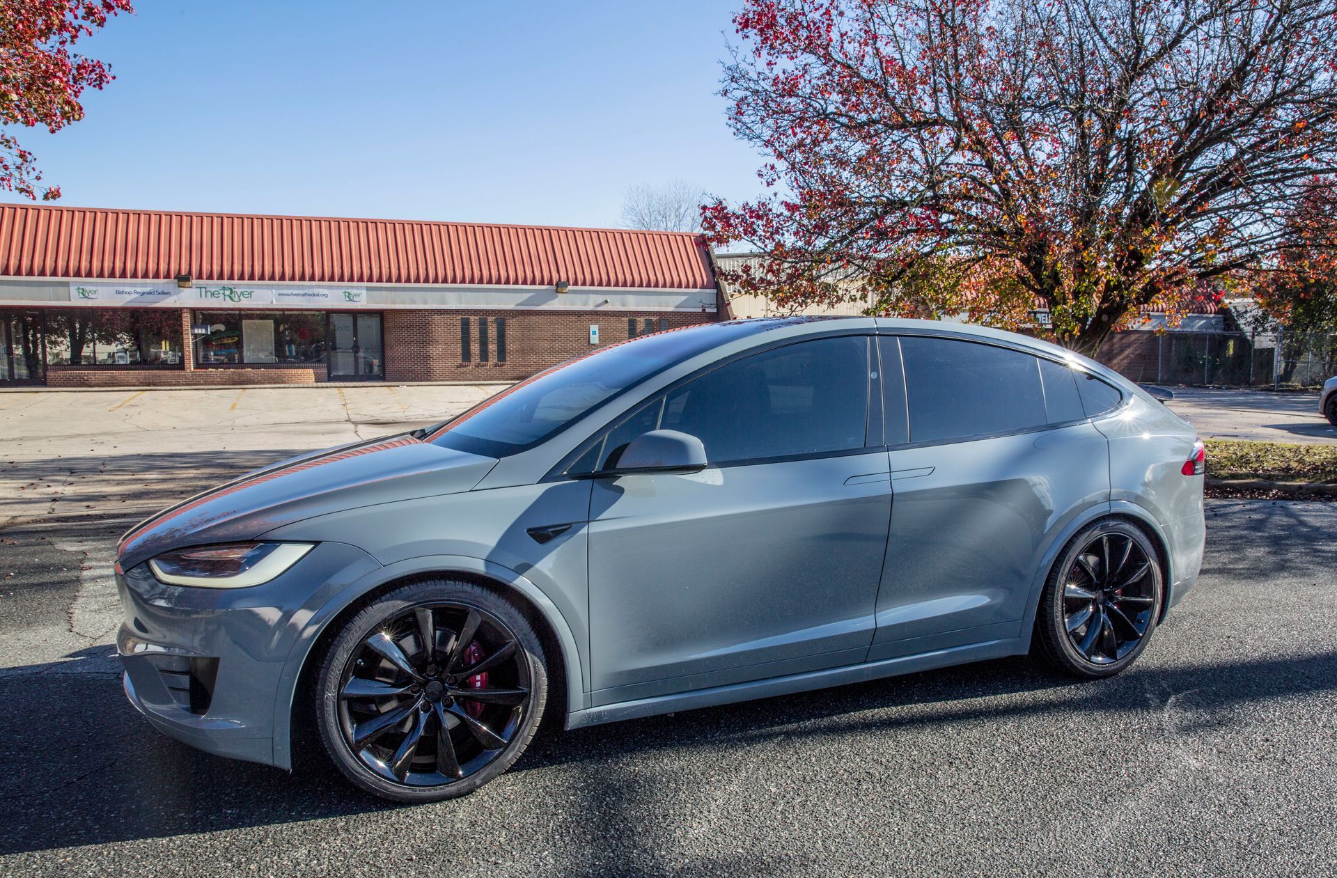 A tesla model x is parked on the side of the road in front of a building.