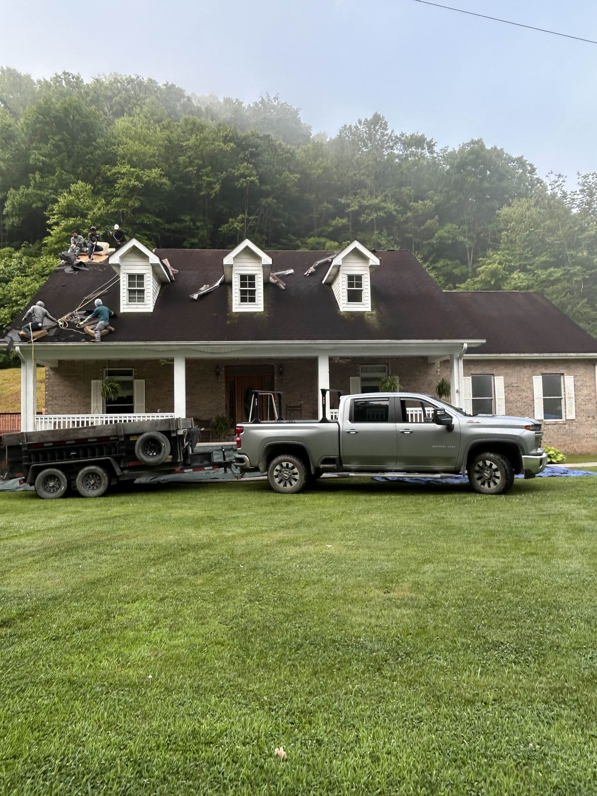Truck pulling trailer in front of a house. Roofers working on the roof on a foggy day.