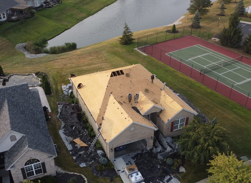 House under roof construction with tennis court and pond in the background.
