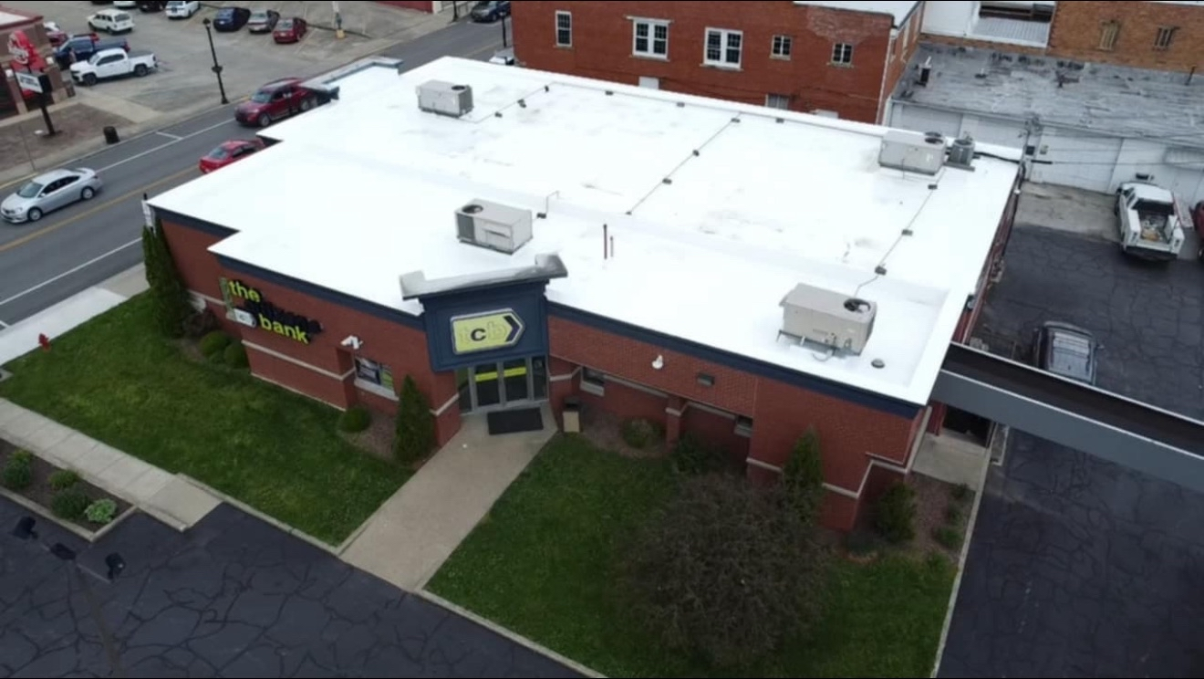 Aerial view of a one-story brick building with a white roof and green lawn.