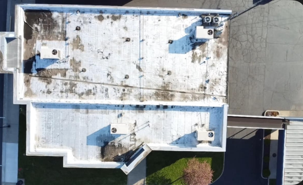 Overhead view of a flat commercial roof with multiple HVAC units and visible weathering.