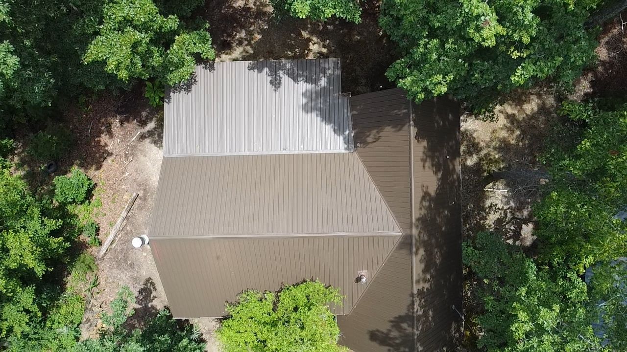 Overhead view of a house with a brown roof surrounded by green trees.