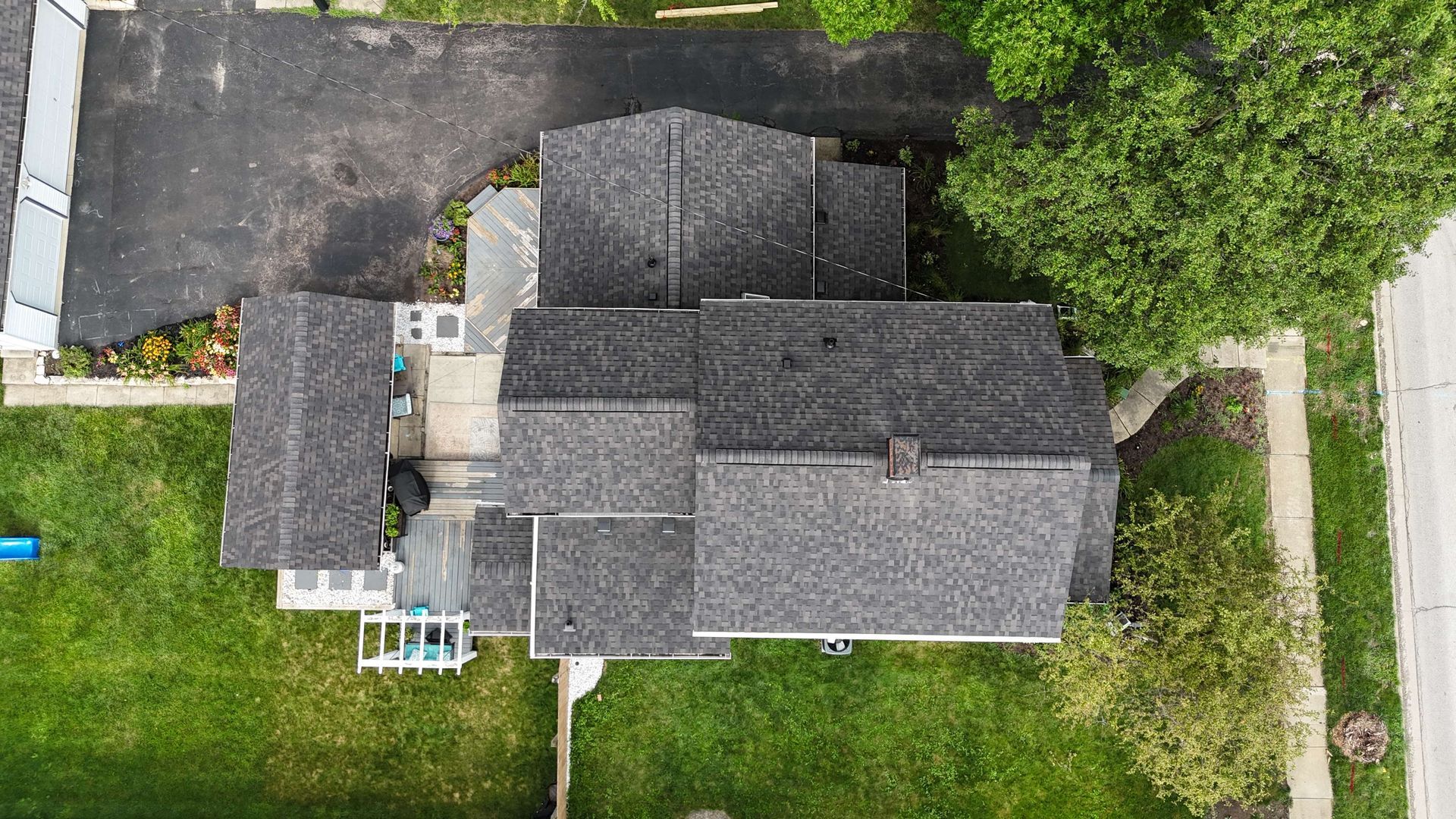 Overhead view of a house with a dark roof and a driveway, surrounded by green grass and trees.