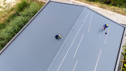 Building with dark gray corrugated roof and black gutters. Yellow exterior, windows.