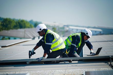 Two workers in safety gear installing solar panels on a rooftop.